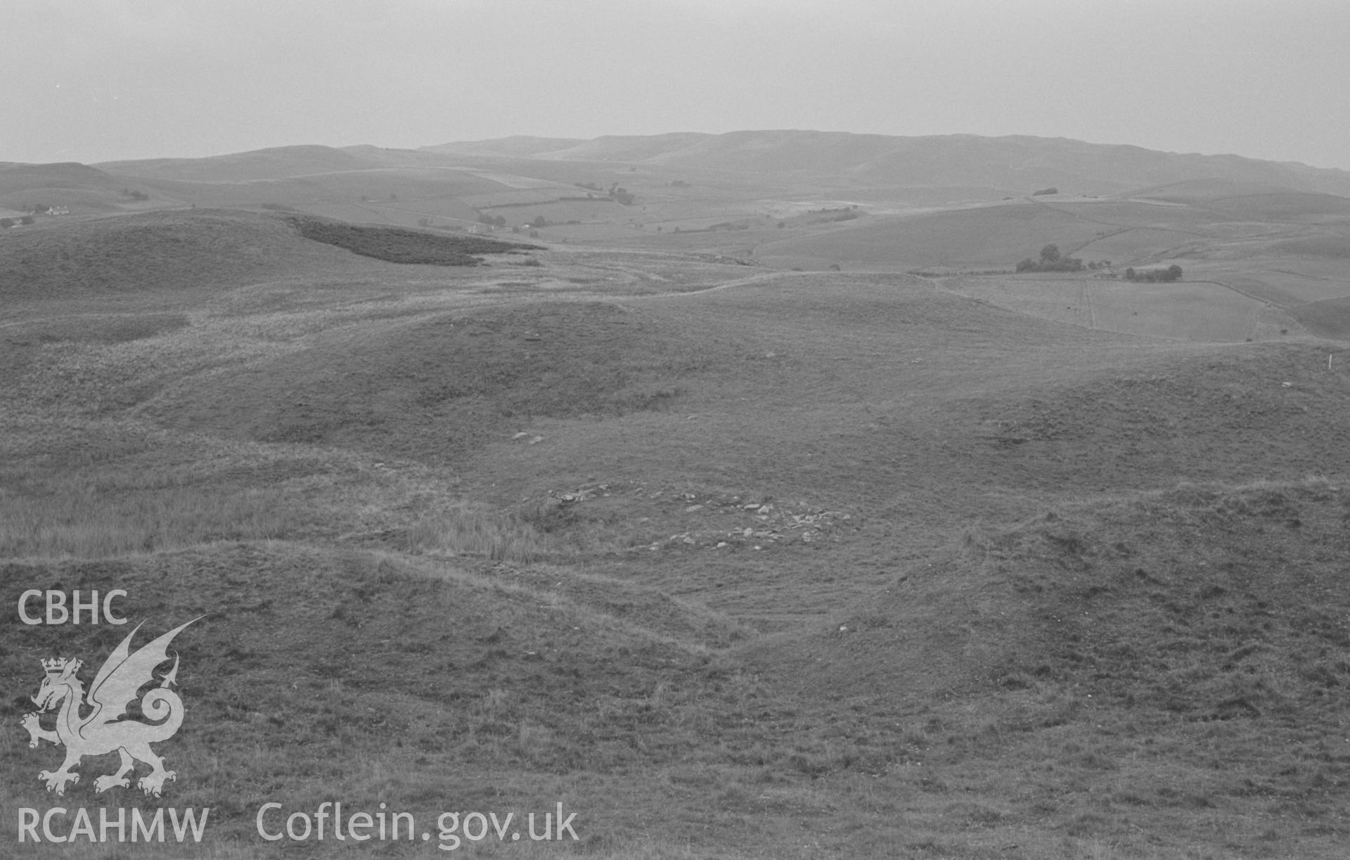 Digital copy of black & white negative showing view looking north east across the entrance of Pen y Bannau iron age camp to the remains of the foundation of a small building 50m north east. Photographed by Arthur O. Chater on 25th August 1967, SN 742 669.
