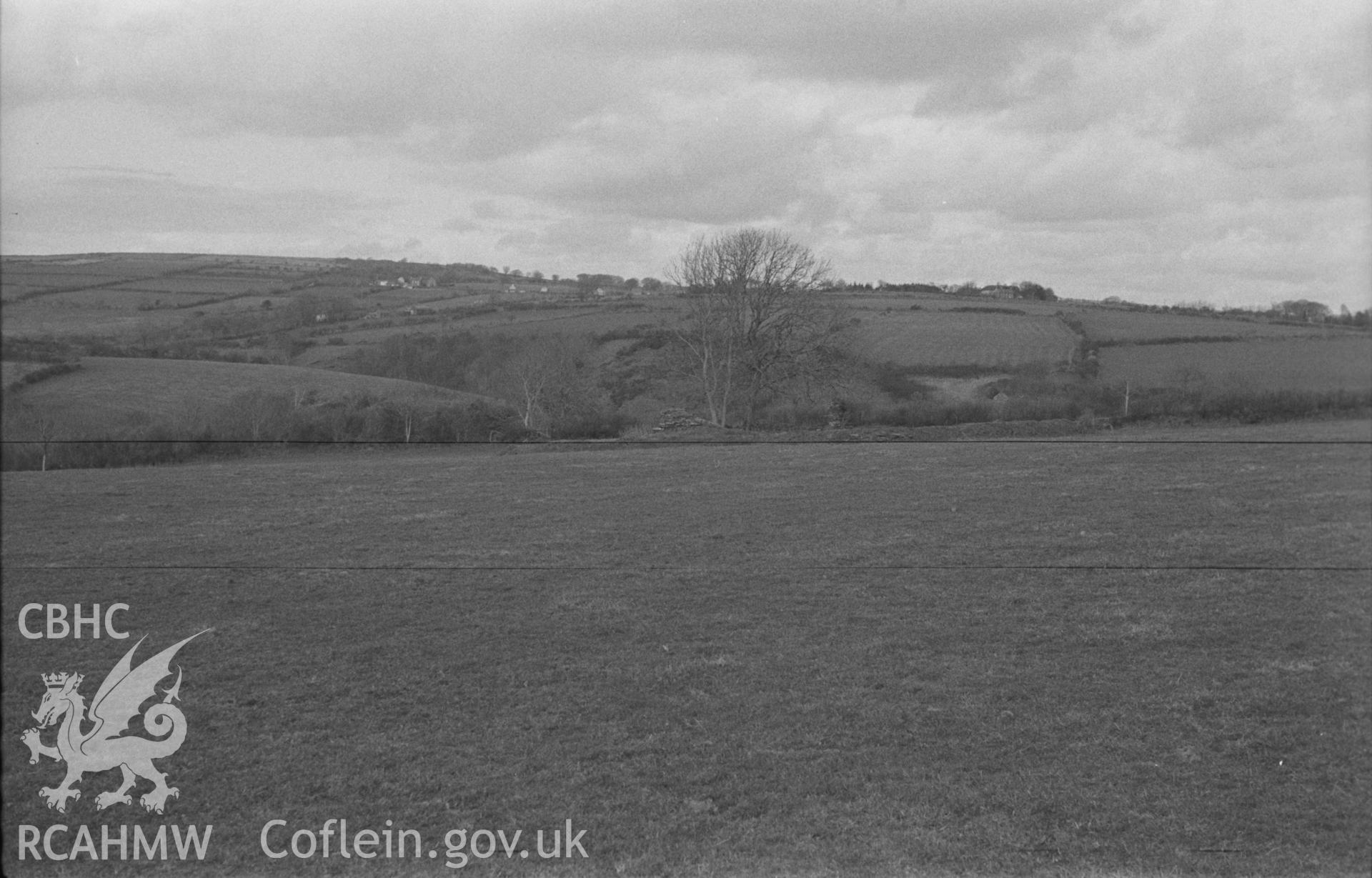Digital copy of a black and white negative showing site of St Mary's church, Llanfair Trefhelygen, with the houses of Coed-y-Bryn in the distance. Photographed in April 1963 by Arthur O. Chater from Grid Reference SN 3430 4403, looking north east.
