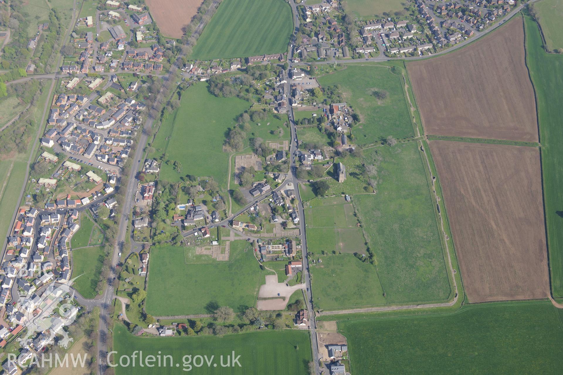 Caerwent village and Roman city including views of the Roman Amphitheatre and Basilica and Forum; Motte; St. Stephen's Church; Caerwent Baptist Chapel; Caerwent Institute Caerwent House; Great House and West Gate Farm. Oblique aerial photograph taken during the Royal Commission's programme of archaeological aerial reconnaissance by Toby Driver on 21st April 2015.