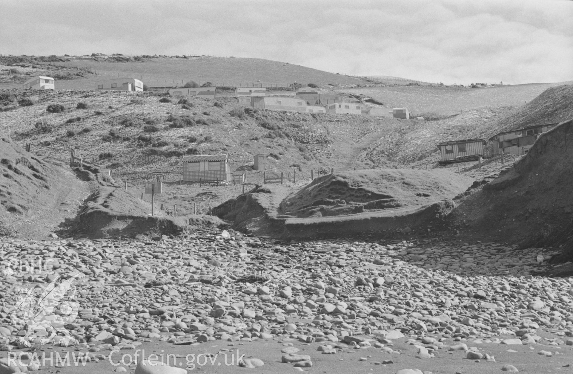 Digital copy of a black and white negative showing caravans, chalets and old train carriages at Pen-y-Graig bay, Upper Borth. Photographed by Arthur O. Chater on 2nd April 1968, looking south east from the beach at Grid Reference SN 600 883.
