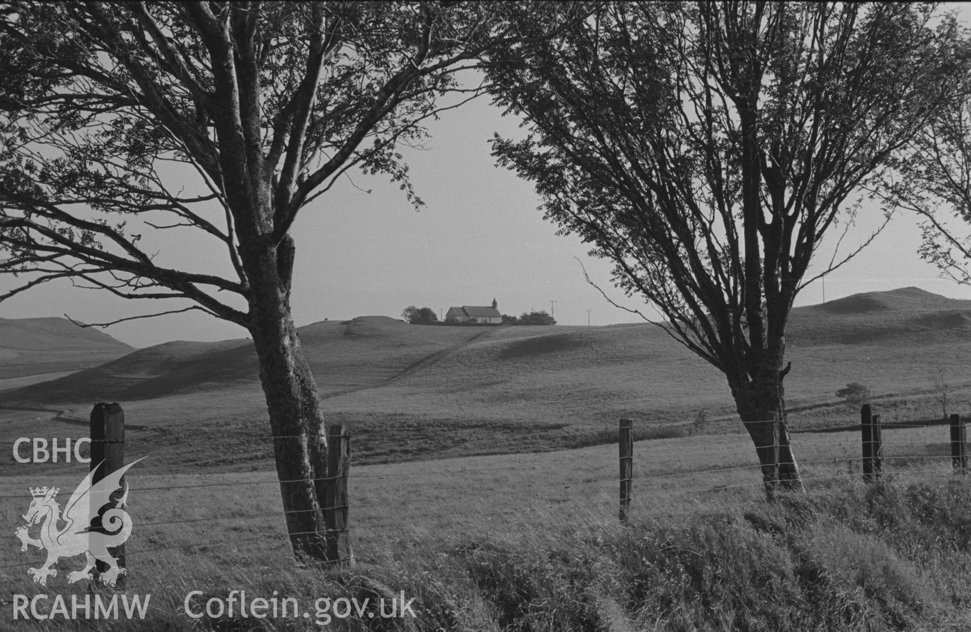 Digital copy of a black and white negative showing distant view of Llantrisant church in the evening light. Photographed by Arthur O. Chater in September 1966 looking south south west from the road to Devil's Bridge at Grid Reference SN 727 754.