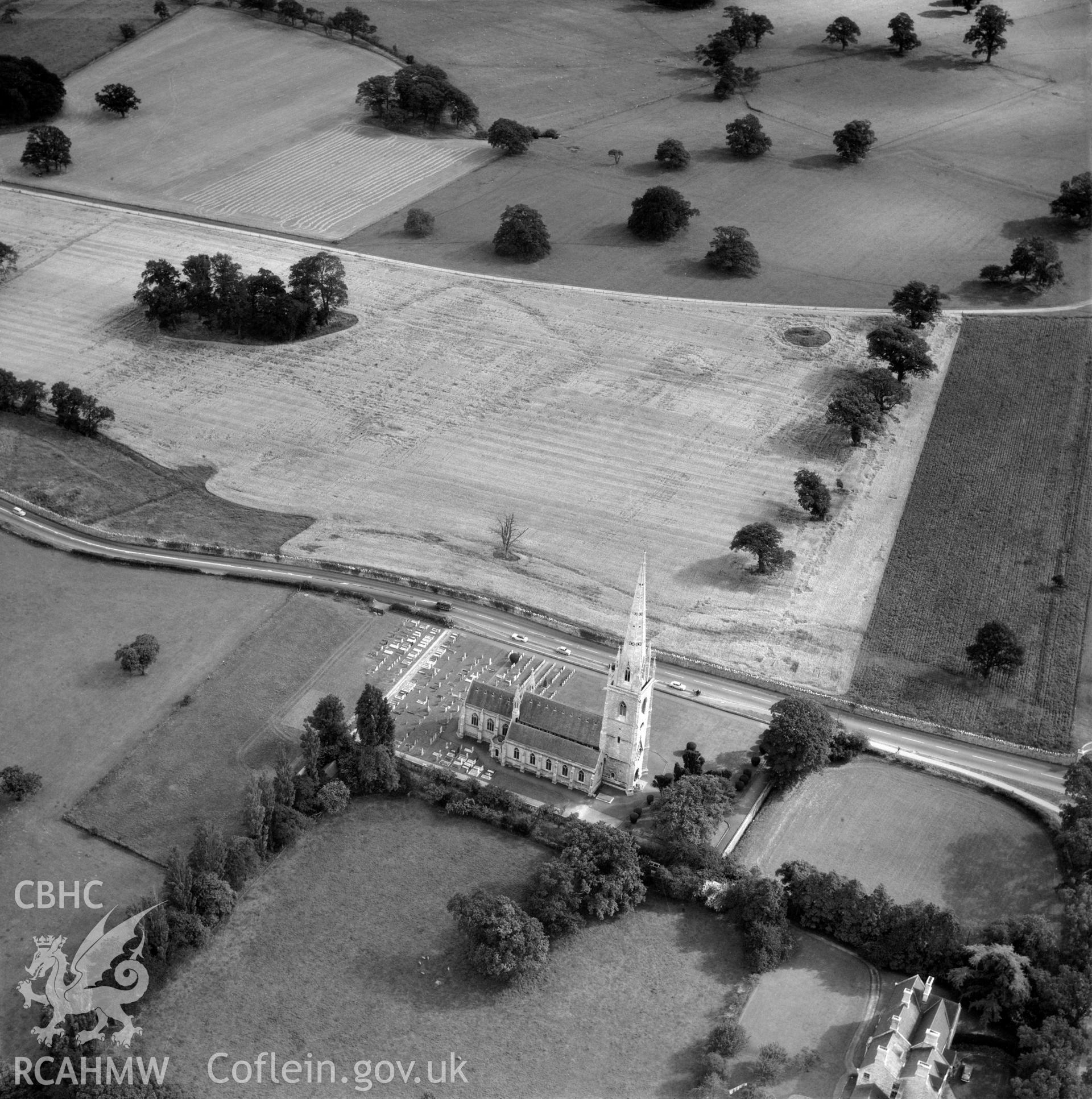 Digital copy of a black and white, oblique aerial photograph of the Marble Church, Bodelwyddan. The photograph shows a view from the North West, showing the cropmark of a prehistoric defended enclosure in the field to the South East.