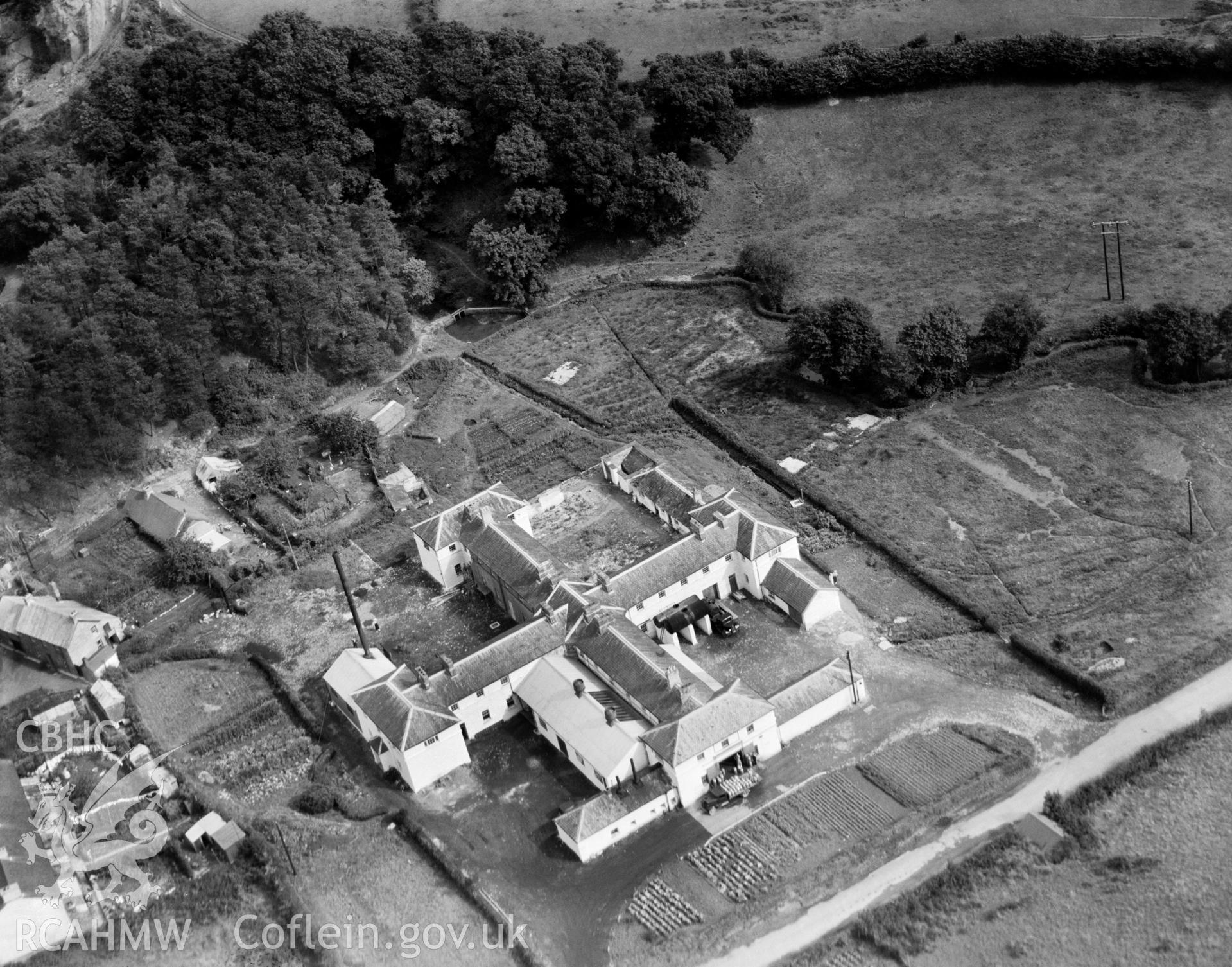 Digital copy of a black and white, oblique aerial photograph of a cheese factory, Newcastle Emlyn. The photograph shows a view from the West. The cheese factory was established in the former town workhouse in 1920 to serve the major dairying area of West Wales.