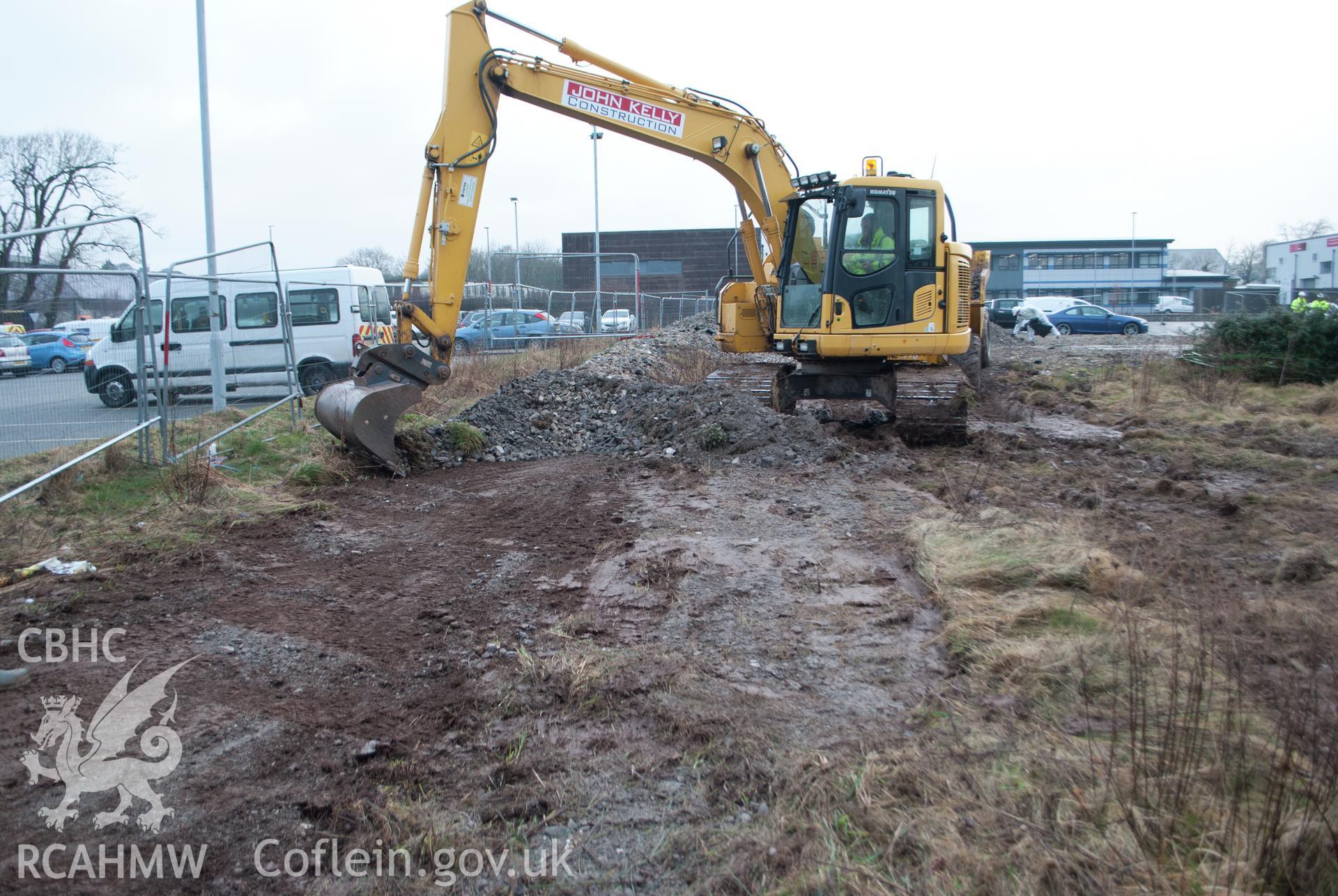 Working shot showing view from the south east at the start of the topsoiling phase - removing crushed stone. Photographed by Gwynedd Archaeological Trust during archaeological watching brief at Pen-yr-Orsedd, Llangefni industrial estate, on 7th March 2018.