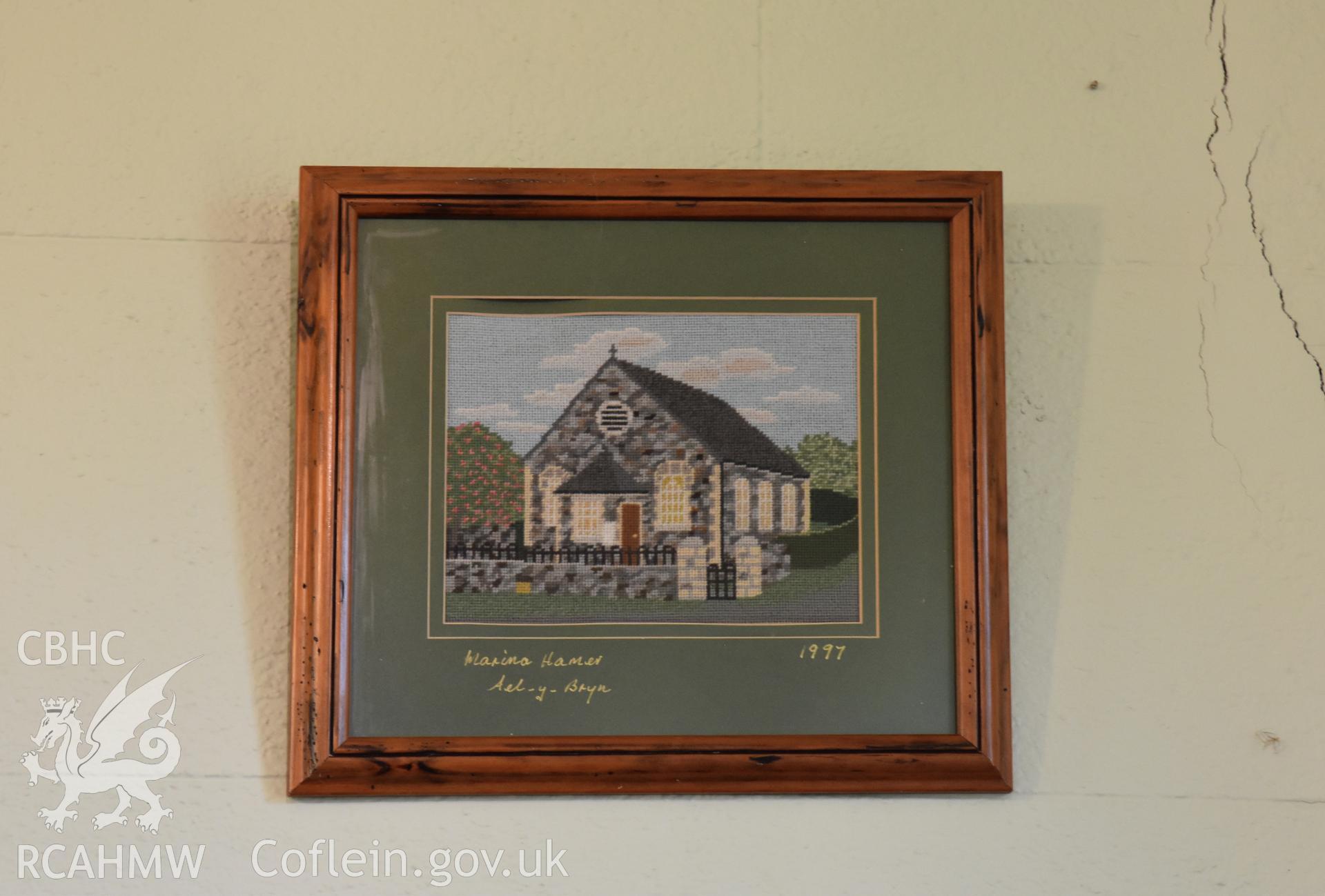 Colour photograph showing framed tapestry of Hyssington Chapel, signed 'Marina Hamer, Ael-y-Bryn 1997' at Hyssington Primitive Methodist Chapel, Hyssington, Churchstoke. Photographic survey conducted by Sue Fielding on 7th December 2018.