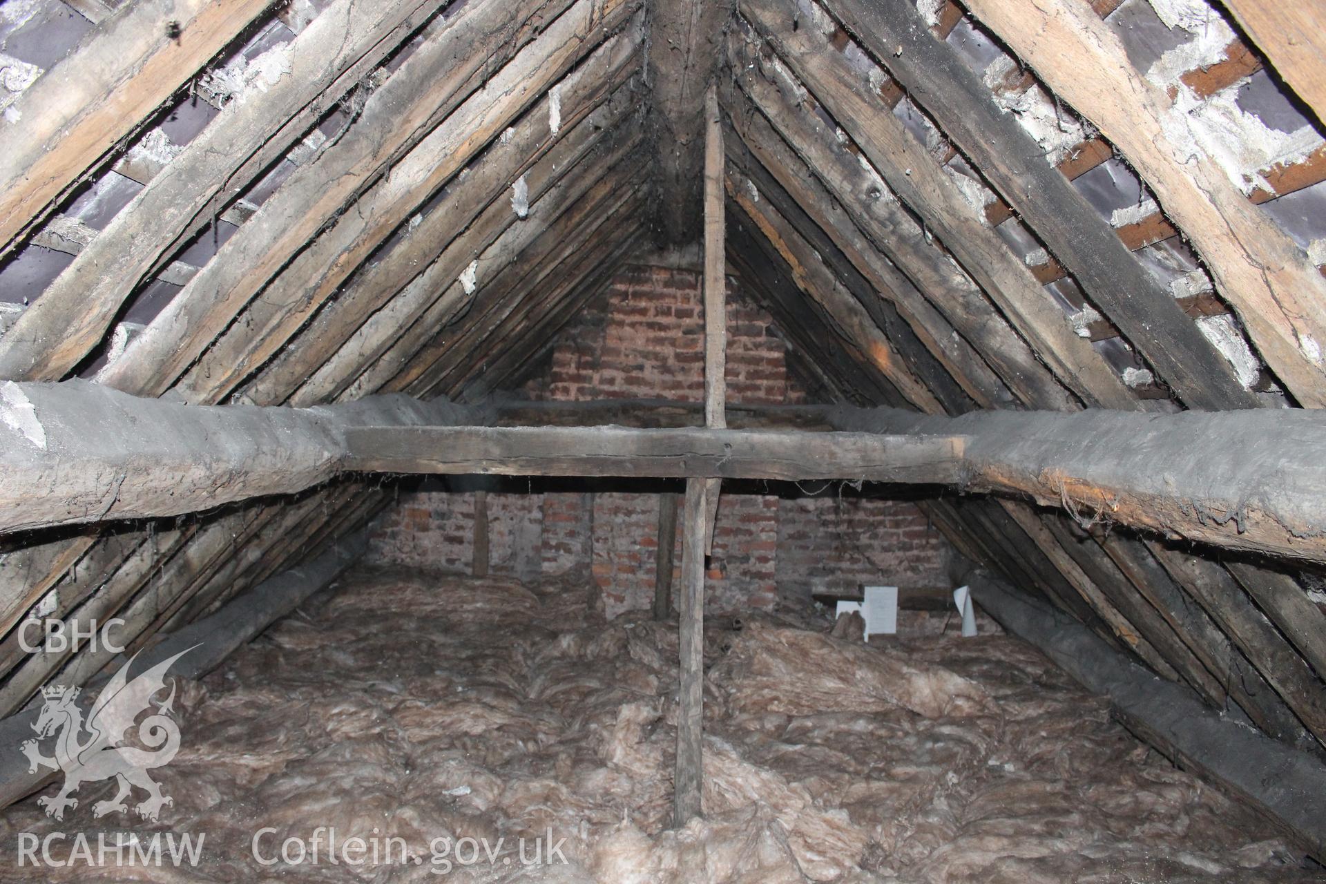 Colour photograph showing detail of timber frame and interior of roof with red brick wall behind, in attic at 5 to 7 Mwrog Street, Ruthin. Photographed during survey conducted by Geoff Ward on 30th May 2014.