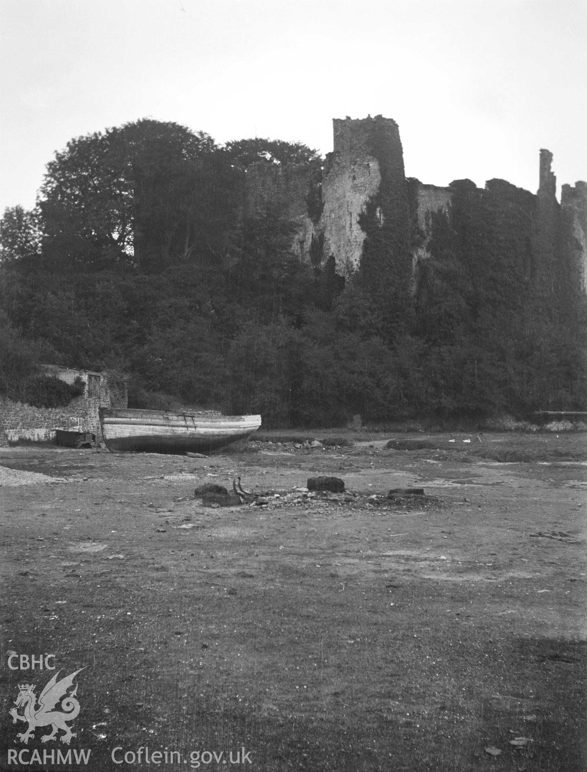 Digital copy of a nitrate negative showing exterior view of Laugharne Castle with a boat in the foreground. From the National Building Record Postcard Collection.