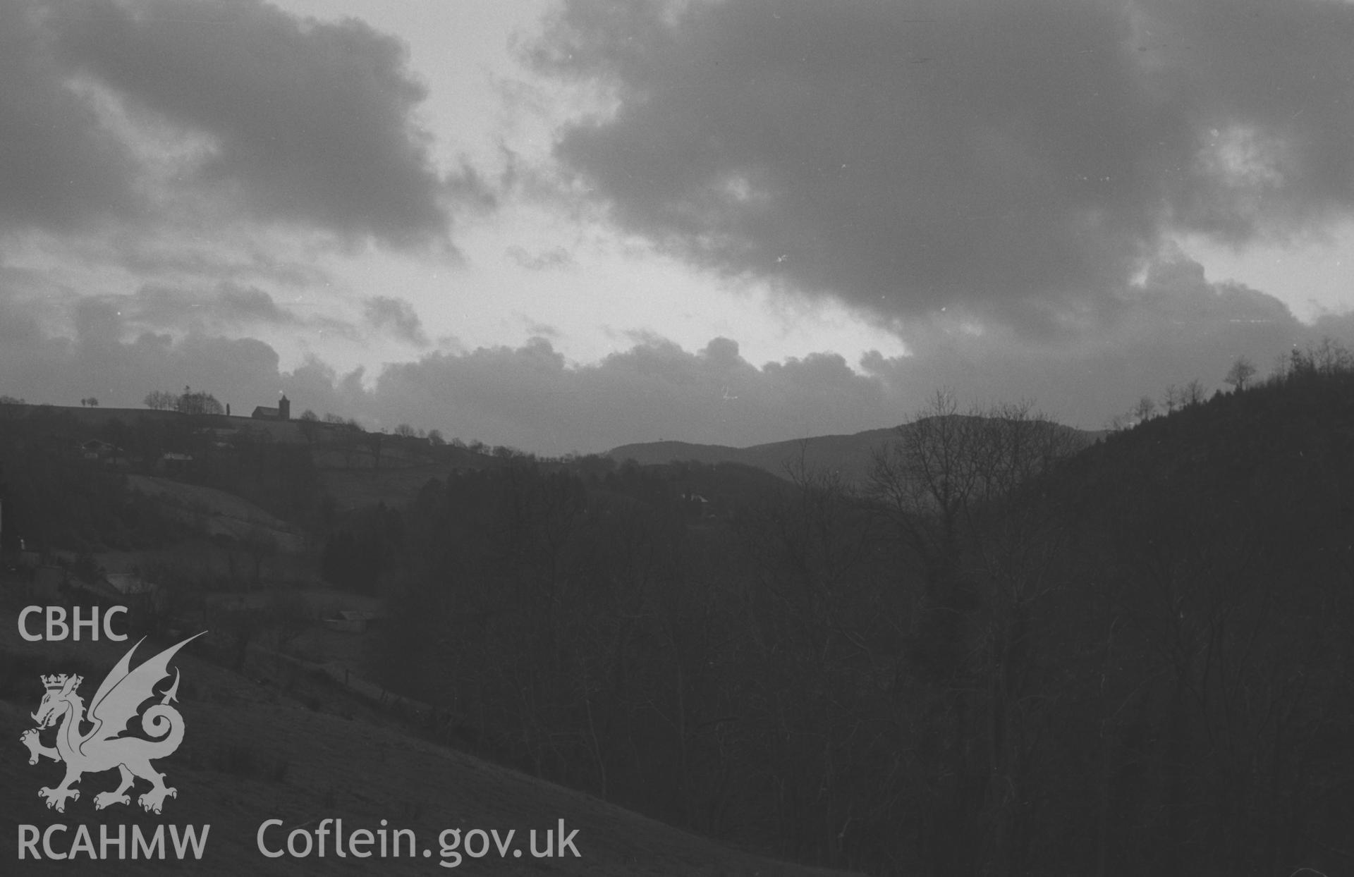 Digital copy of a black and white negative showing distant view of Ysbyty Ystwyth including church on skyline. Photographed by Arthur O. Chater in April 1965 from Pontrhydygroes, Grid Reference SN 739 725, looking south west.