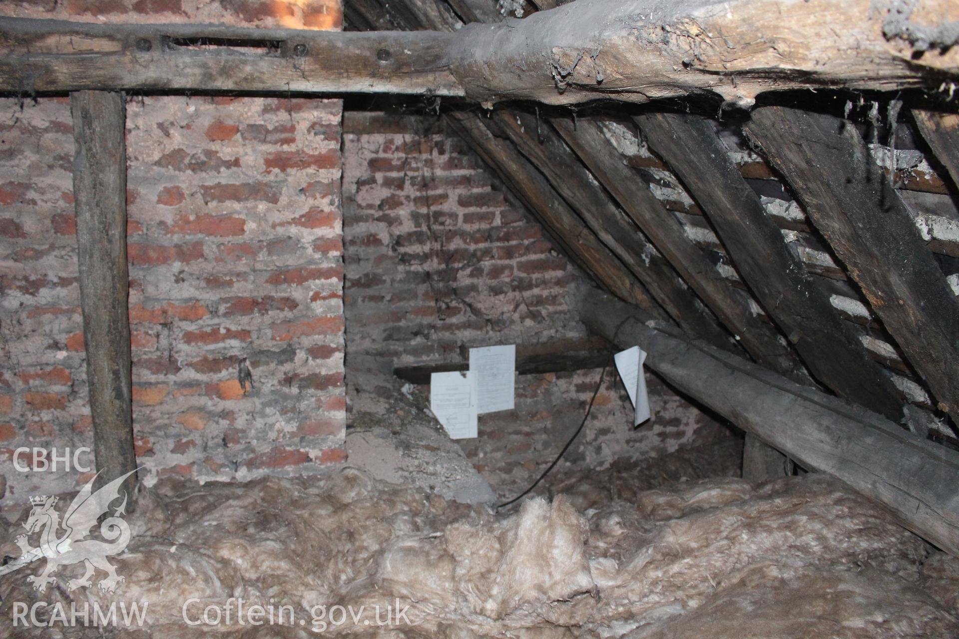 Colour photograph showing detail of timber frame, interior of roof and red brick chimney stack and wall in attic at 5 to 7 Mwrog Street, Ruthin. Photographed during survey conducted by Geoff Ward on 30th May 2014.