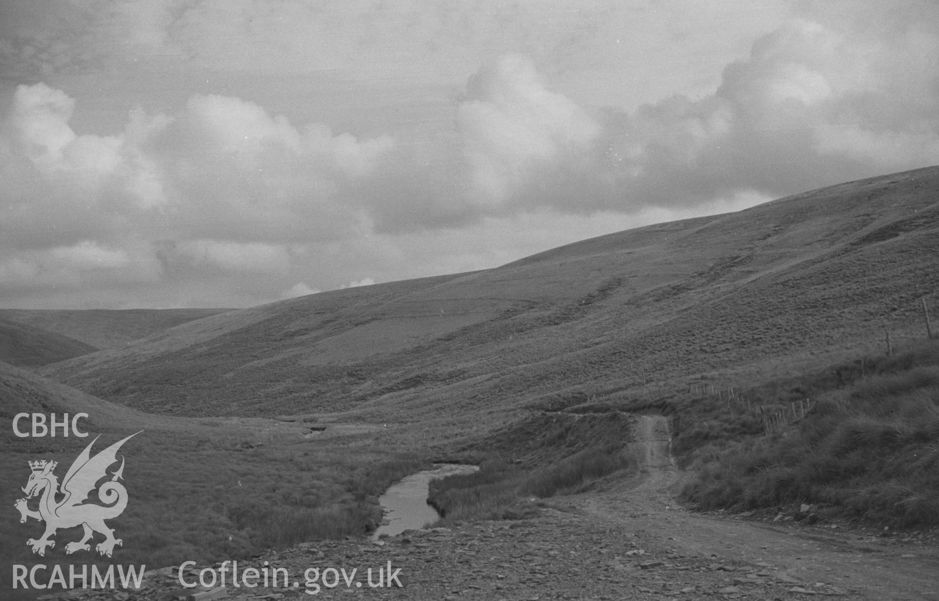 Digital copy of a black and white negative showing view down the Tywi Fechan with the old road on the right, from where the new forestry road crosses the stream. Photographed by Arthur O. Chater in August 1965, looking south east from Grid Ref SN 800 613.