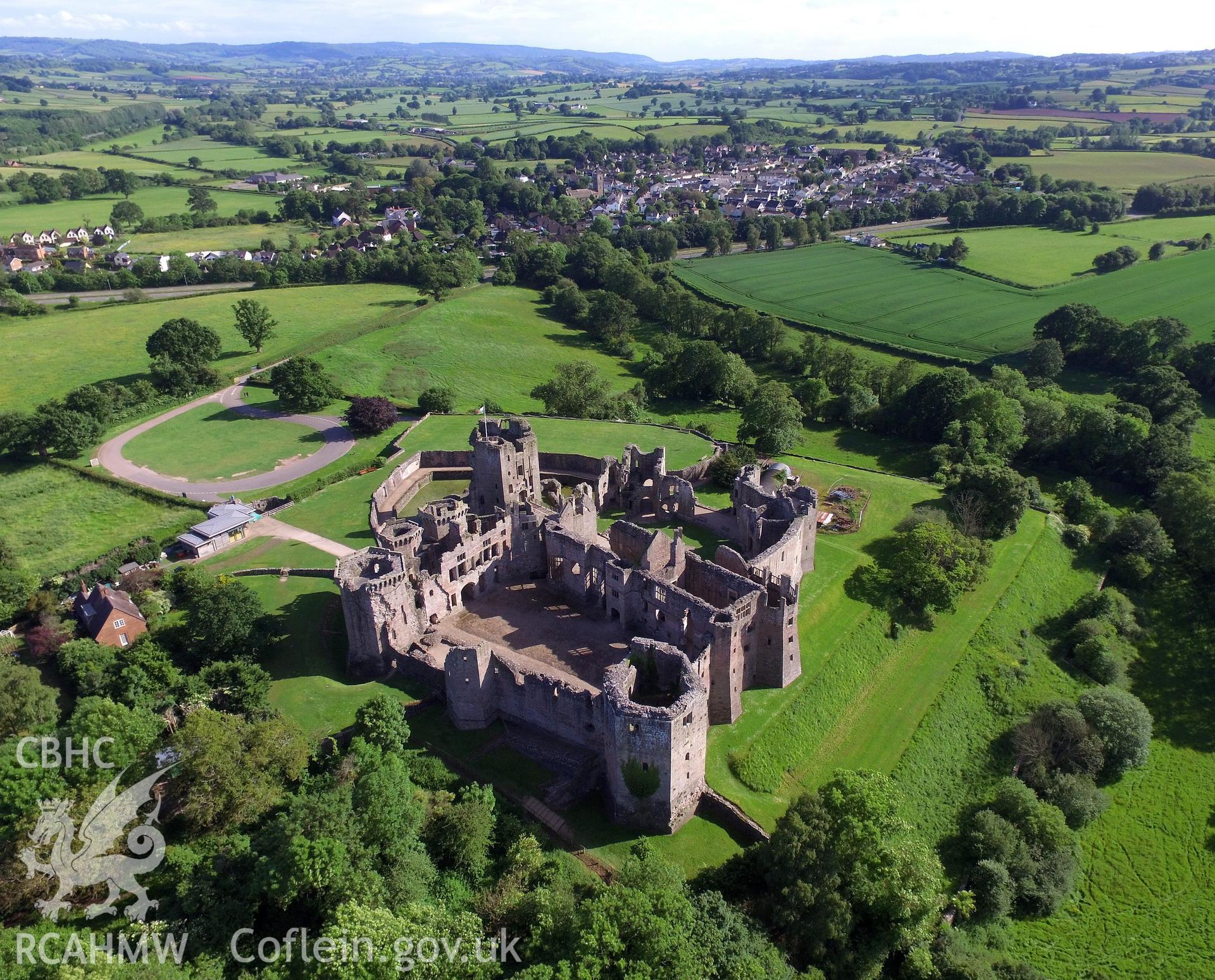 Aerial view from the north of Raglan Castle and the village of Raglan beyond. Colour photograph taken by Paul R. Davis on 3rd June 2017.