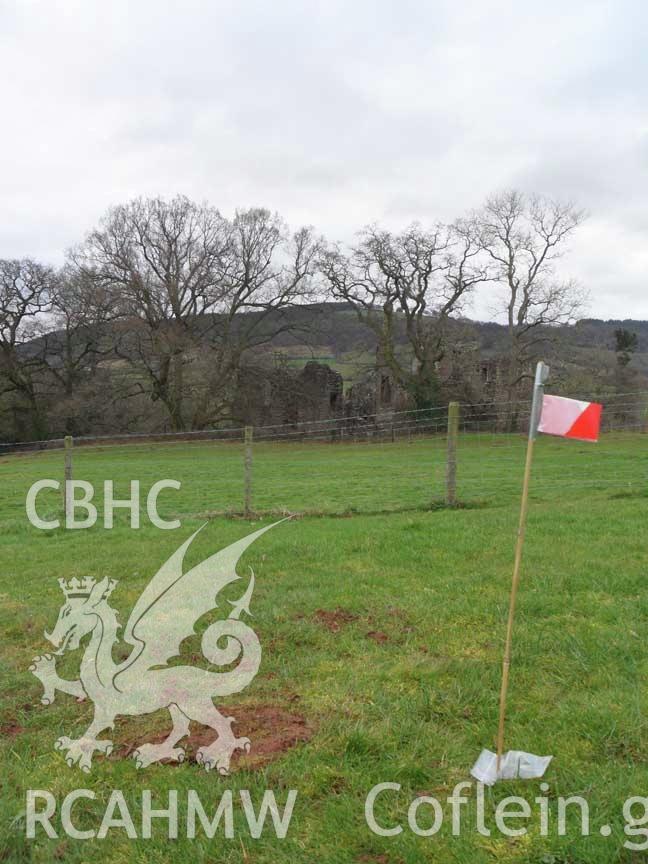 Digital colour photograph of Grosmont battlefield, with Grosmont Castle in the distance, partially hidden by trees. From report no. 1049 - Grosmont battlefield, part of the Welsh Battlefield Metal Detector Survey, carried out by Archaeology Wales.