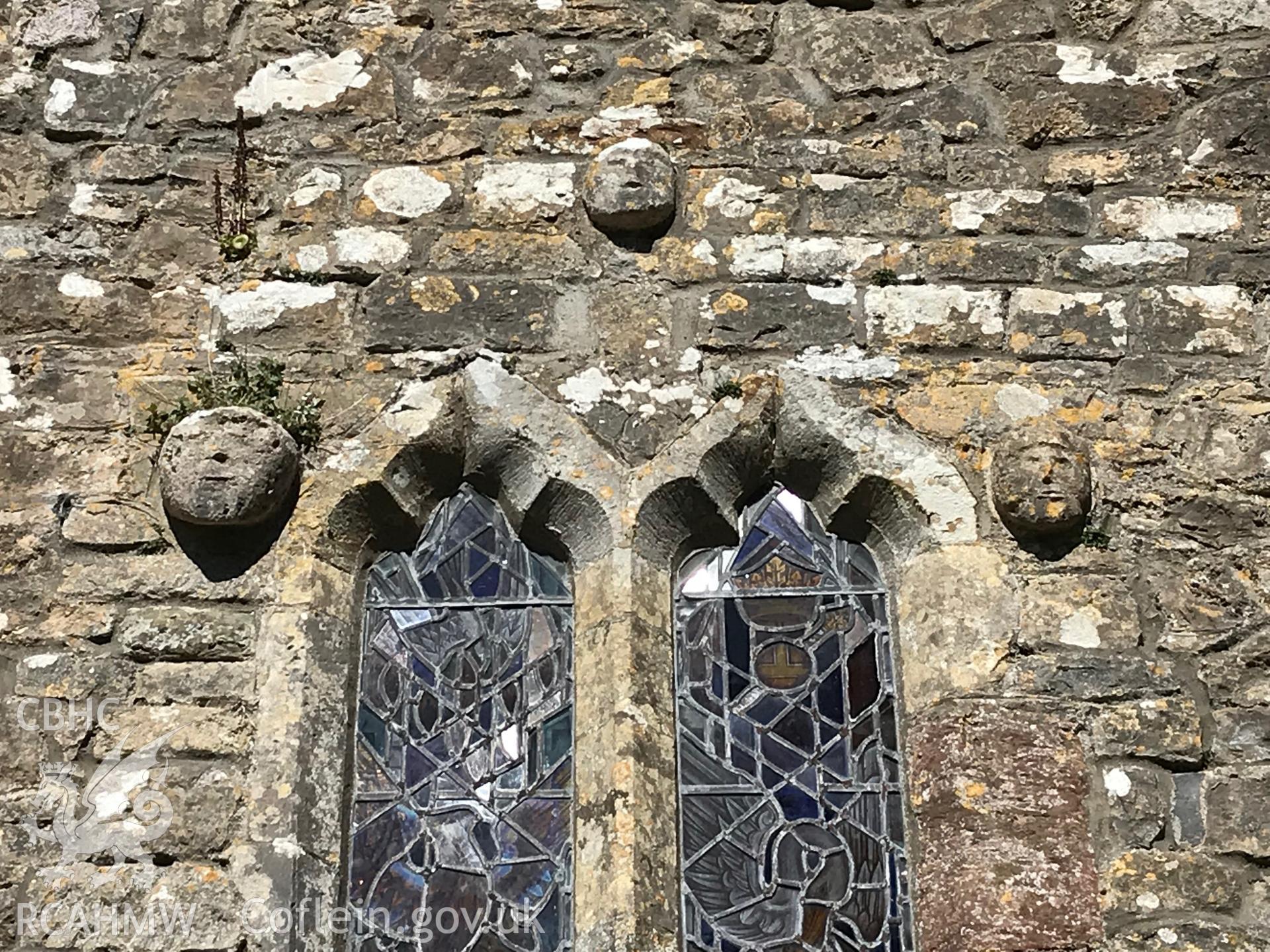 Digital colour photograph showing detailed exterior view of stained glass window and church face carvings at St. Cadog's Church, Cheriton, taken by Paul R. Davis on 5th May 2019.