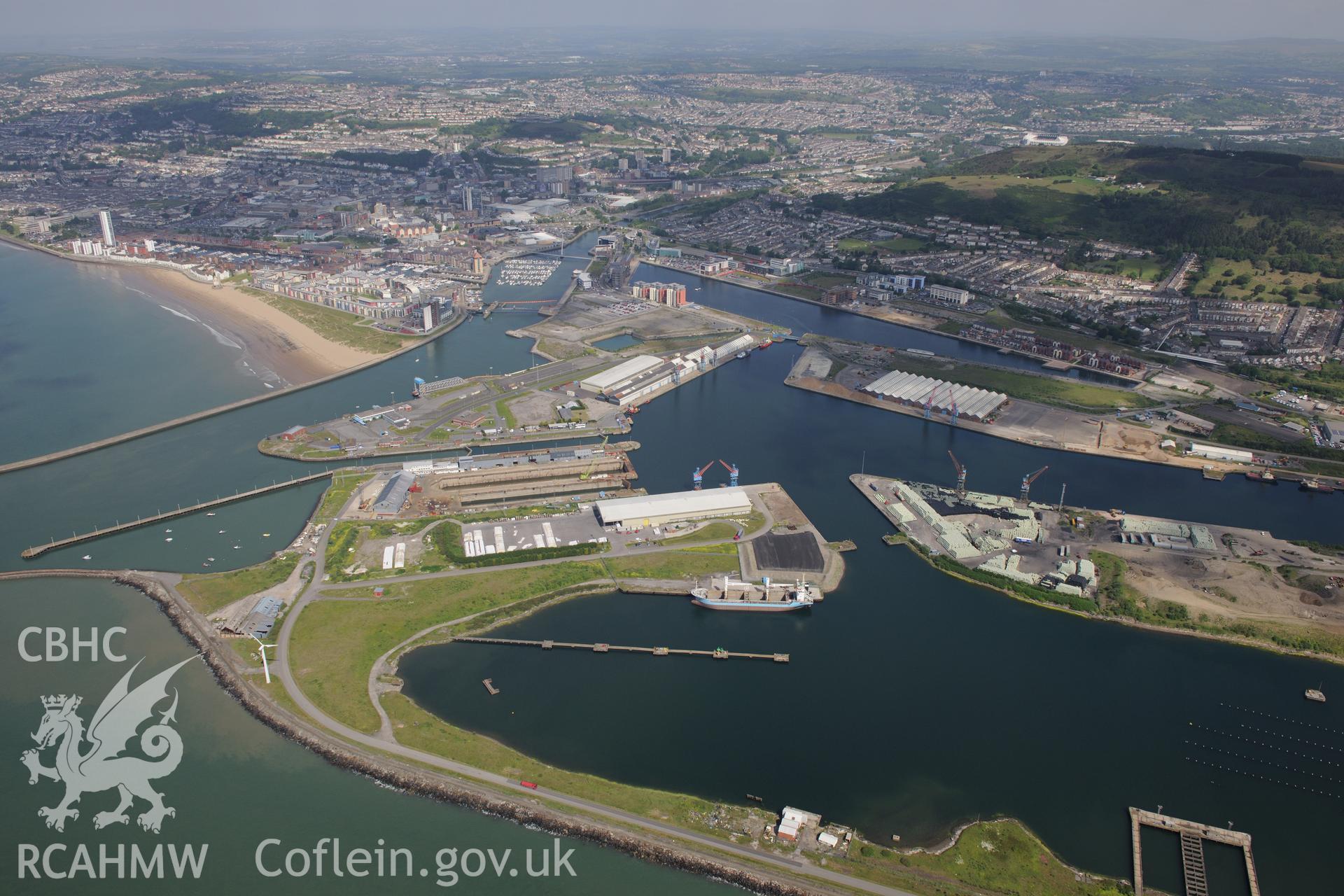 Swansea docks including the King's Dock, Queen's Dock and Prince of Wales Dock, with the city of Swansea in the background and Graigola Merthyr Patent Fuel Works in the foreground. Oblique aerial photograph taken during the Royal Commission's programme of archaeological aerial reconnaissance by Toby Driver on 19th June 2015.