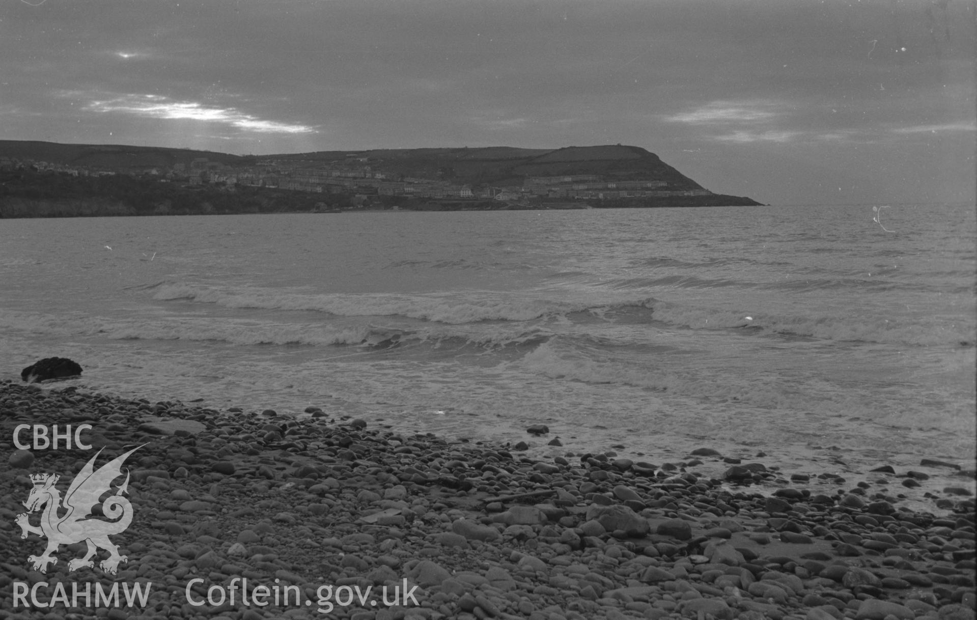 Black and White photograph showing distant view of New Quay Head from the beach at Llanina. Photographed by Arthur Chater in December 1961 from Grid Reference SN 404 599, looking west.