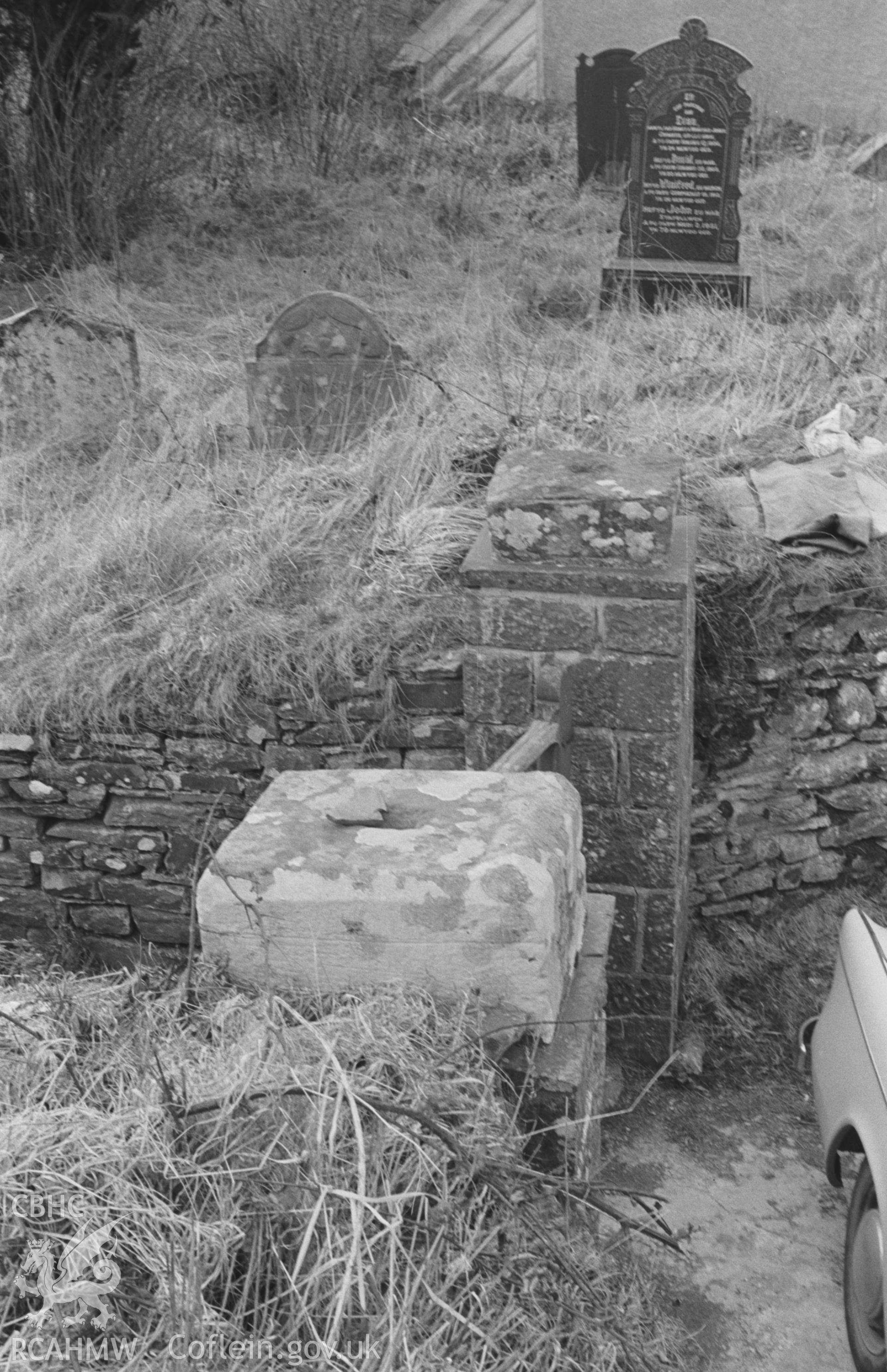 Black and White photograph showing Bowe (upside down on near gatepost) and base (on further gatepost) of Norman font, at north east corner of Lledrod churchyard. Photographed by Arthur Chater in April 1963 from Grid Reference SN646702, looking north-west.