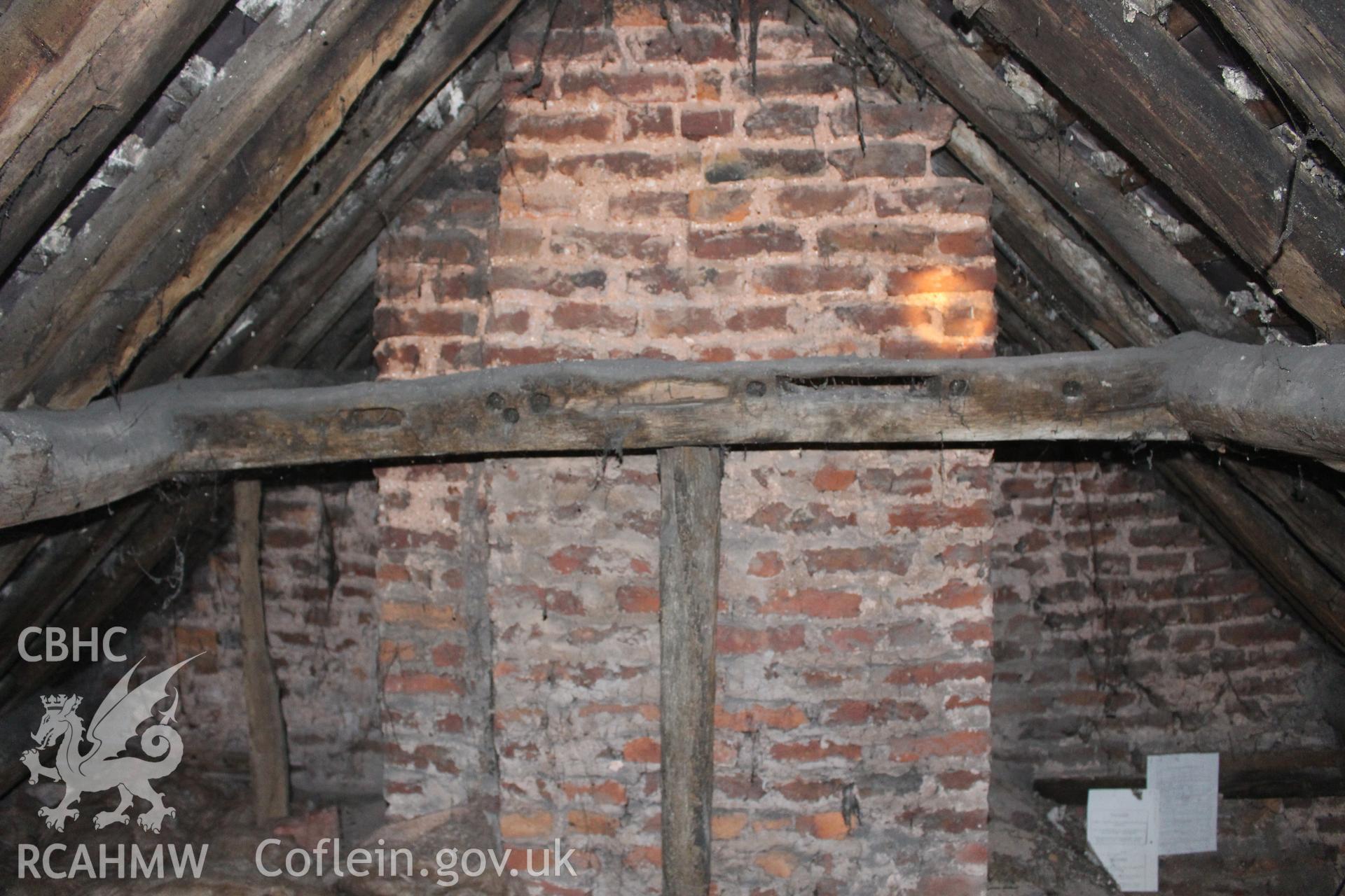 Colour photograph showing detail of timber frame, interior of roof and red brick chimney stack and wall in attic at 5 to 7 Mwrog Street, Ruthin. Photographed during survey conducted by Geoff Ward on 30th May 2014.