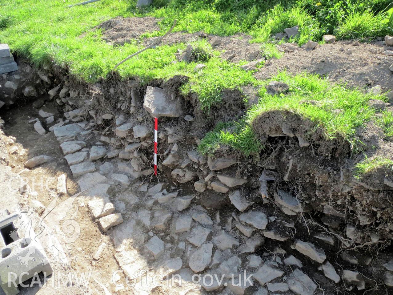 'Oblique view of Sample Section 3, showing stone rubble above in situ foundations. Scales 1x0.5m. Looking South-South-West.' Photographed as part of Archaeological Watching Brief of Upper House Farm, Painscastle, by Archaeology Wales.