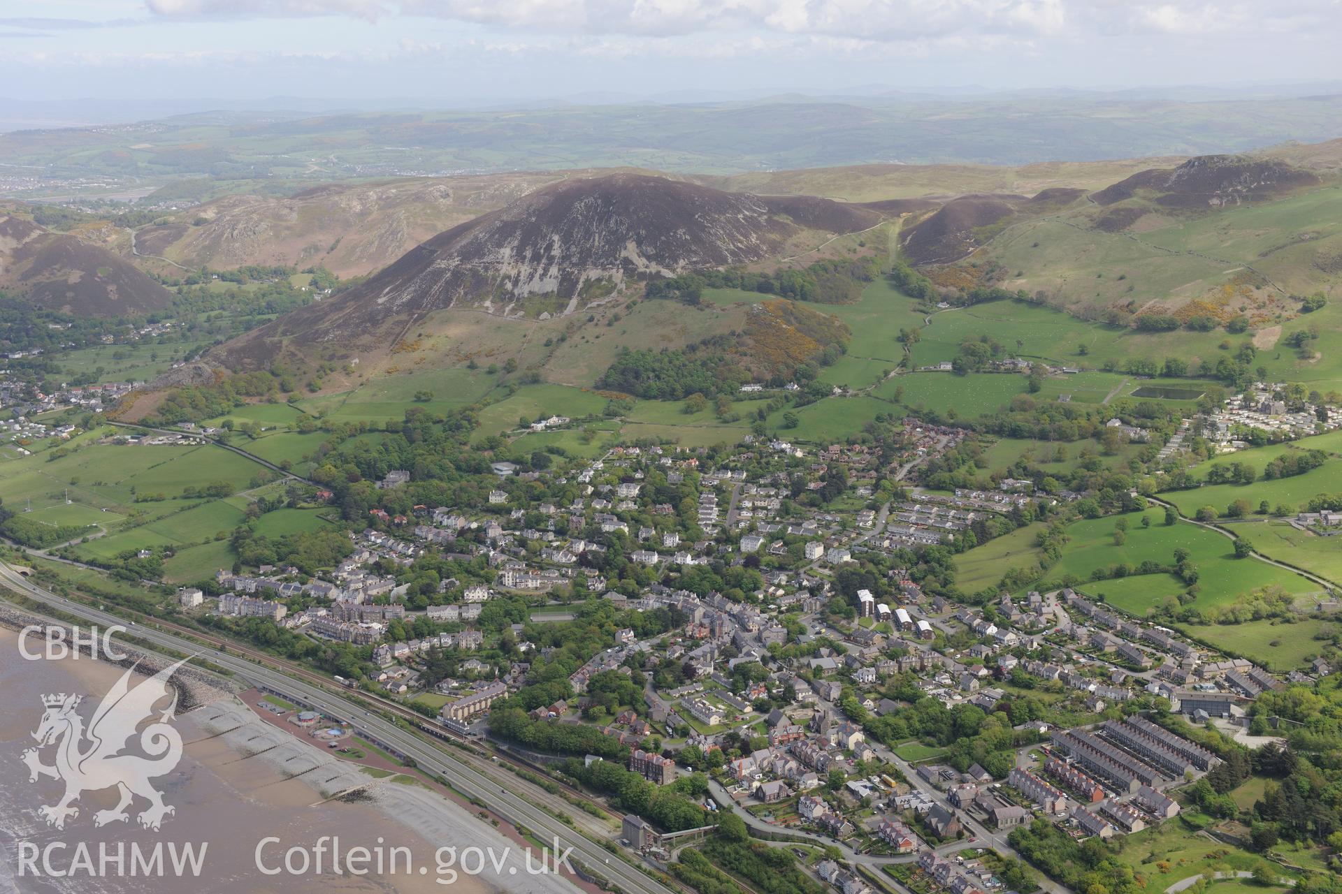 Penmaenmawr town with Foel Lus cairn at the top of the hill beyond. Oblique aerial photograph taken during the Royal Commission?s programme of archaeological aerial reconnaissance by Toby Driver on 22 May 2013.