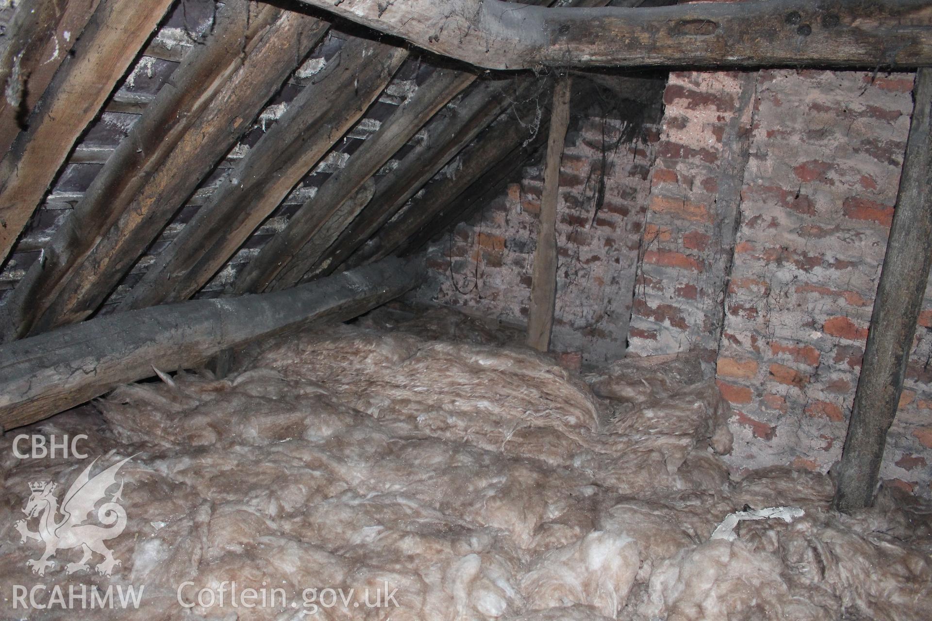 Colour photograph showing detail of timber frame, interior of roof and red brick chimney stack and wall in attic at 5 to 7 Mwrog Street, Ruthin. Photographed during survey conducted by Geoff Ward on 30th May 2014.