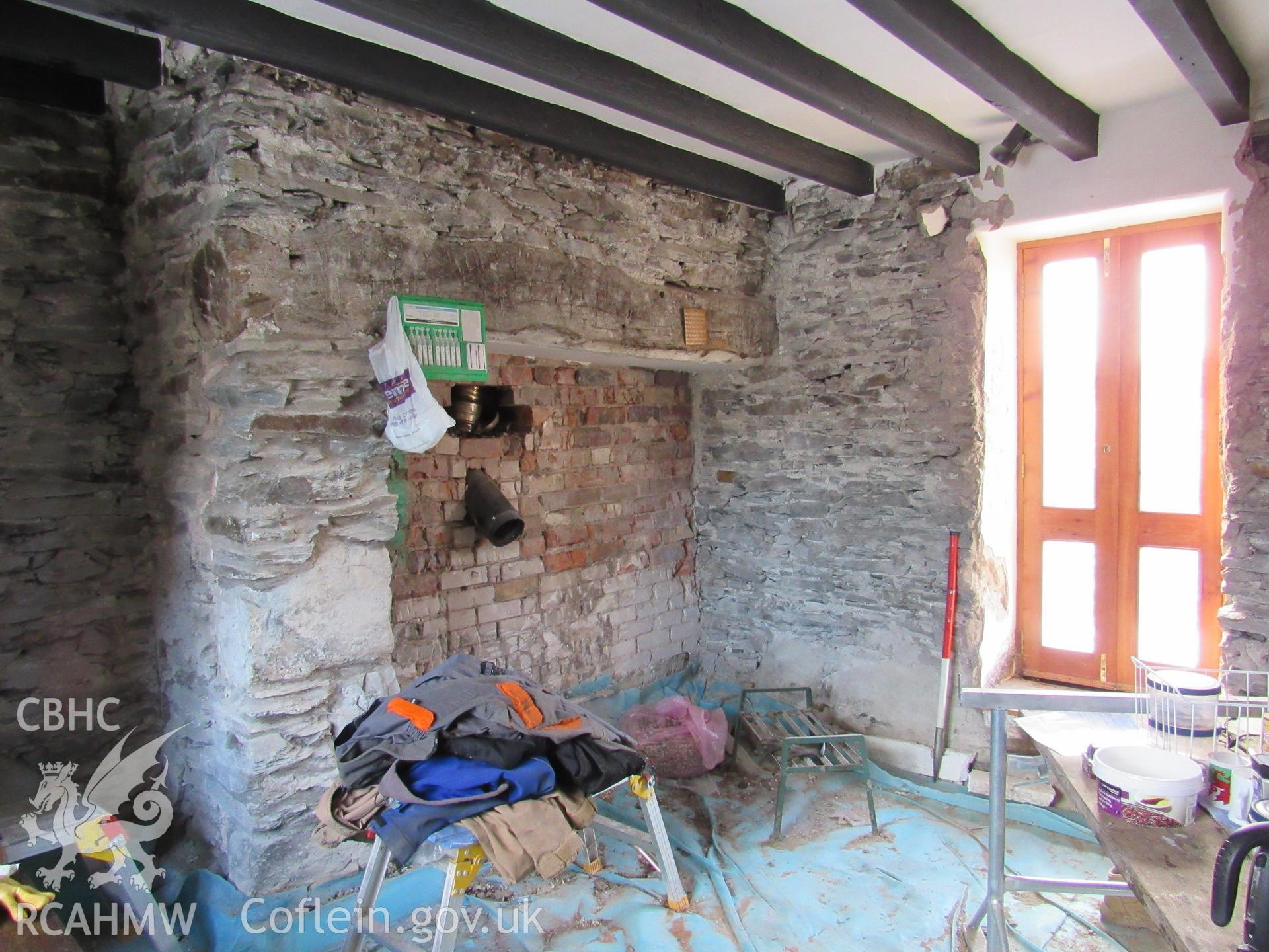 The lounge with fireplace and inserted door, view south. 1m scale. Photographed as part of archaeological building recording conducted at Bryn Ysguboriau, Llanelidan, Denbighshire, carried out by Archaeology Wales, 2018. Project no. P2587.