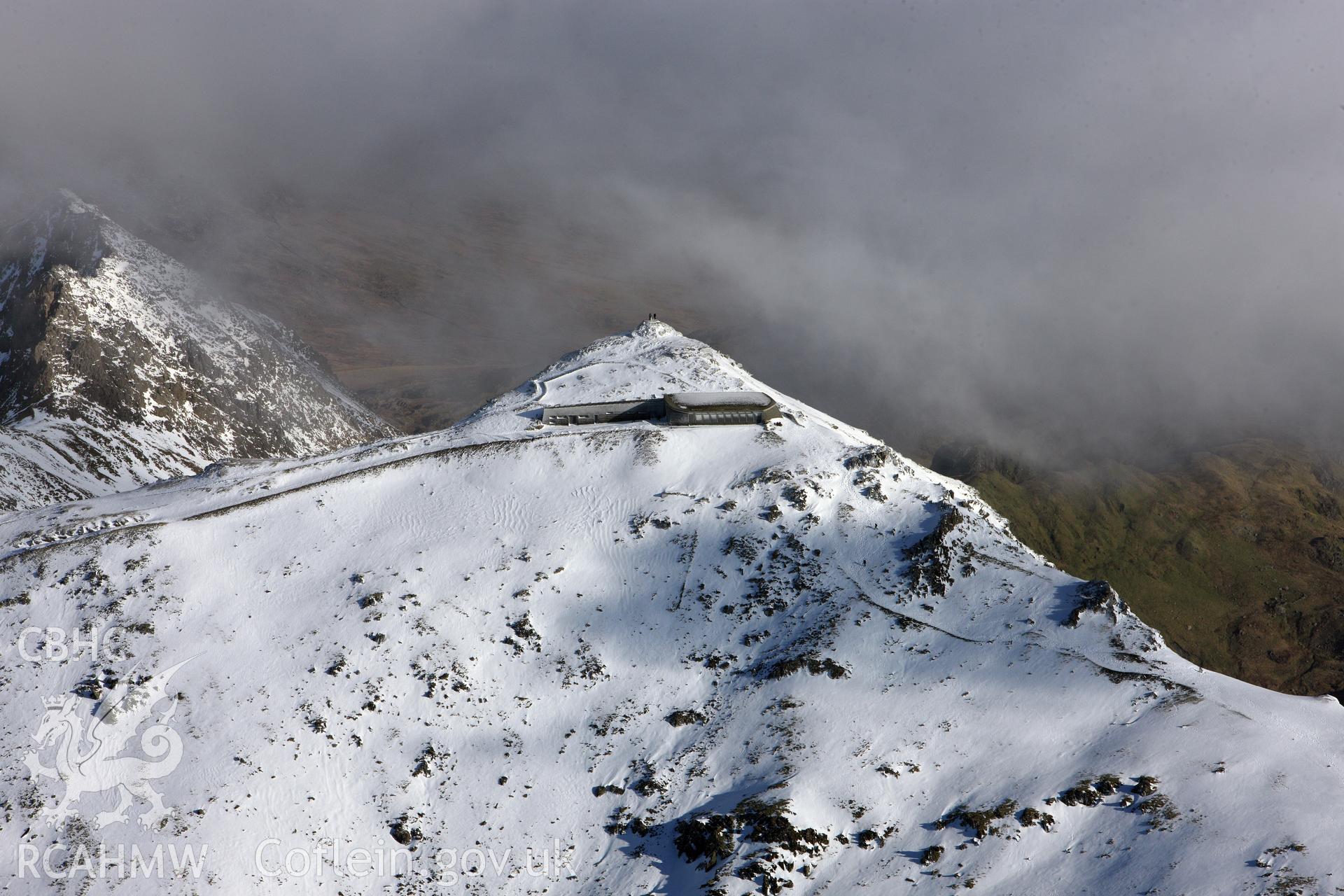RCAHMW colour oblique photograph of Snowdon summit under snow, zoom view from the west with two figures at summit. Taken by Toby Driver on 10/12/2012.