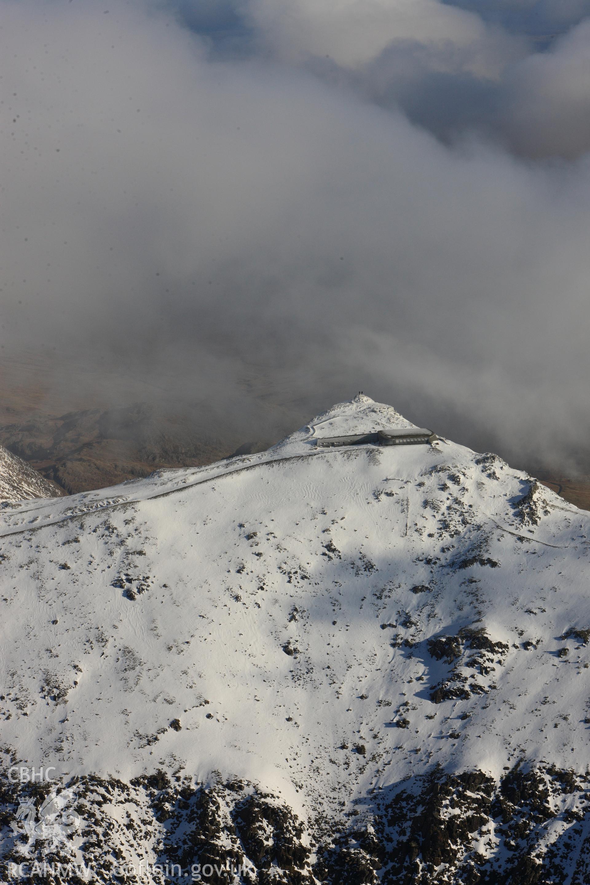 RCAHMW colour oblique photograph of Snowdon summit under snow, zoom view from the west with two figures at summit. Taken by Toby Driver on 10/12/2012.