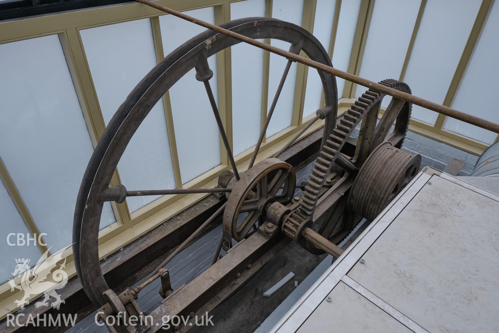 Colour photograph showing Automobile Palace - room 2.1, hoist flywheel and gears, looking W. Produced as part of Historic Building Recording for Automobile Palace, carried out by Richard Hayman, June 2021.