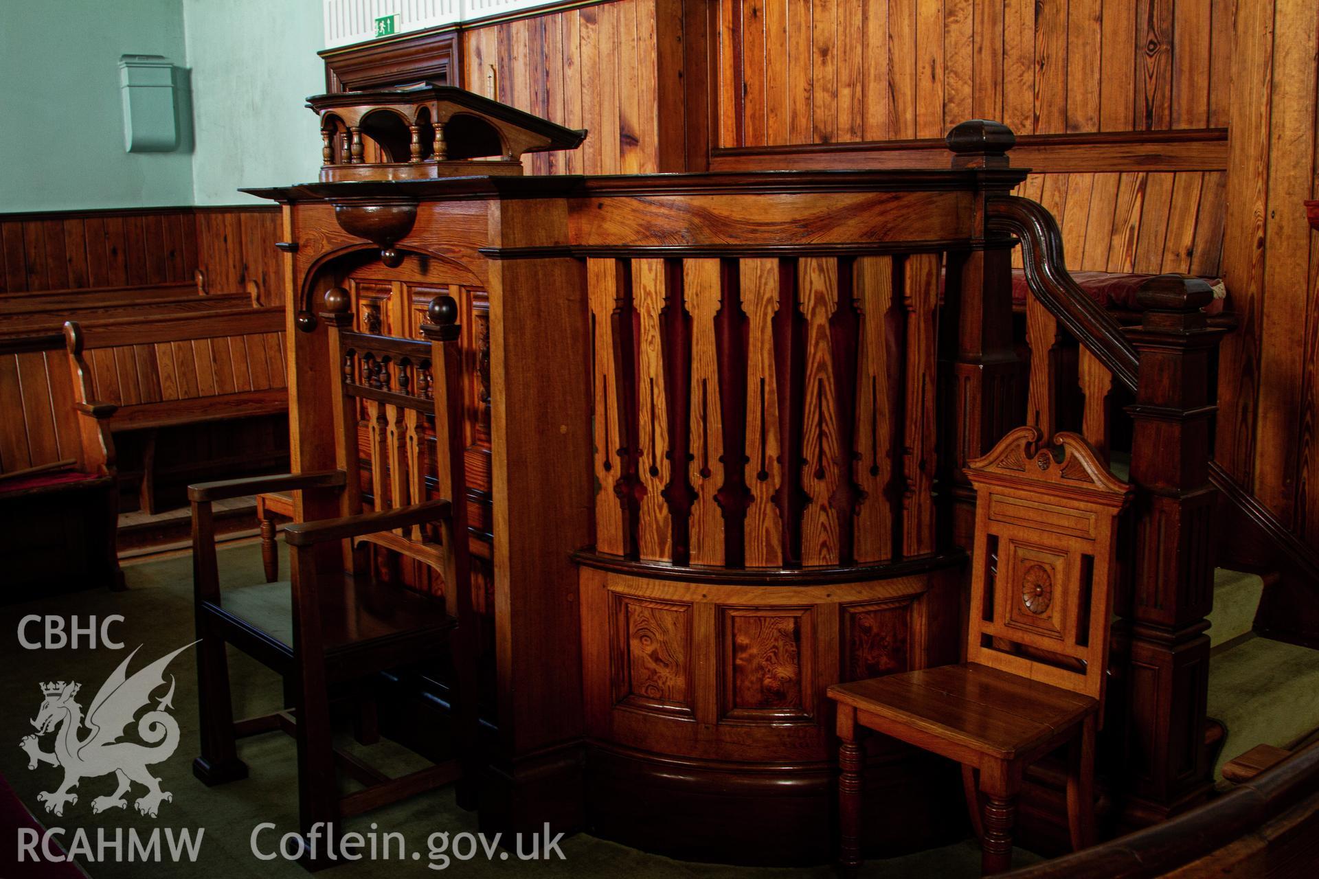 Colour photograph of interior - pulpit, lectern and chapel chairs - part of a photographic survey of Bethania Chapel, Aberangell, Gwynedd, produced for John Linden by Adrian John Hexter, as a condition of planning consent. (Planning Application Ref. No. NP5/74/L319). Snowdonia National Park Planning Authority.