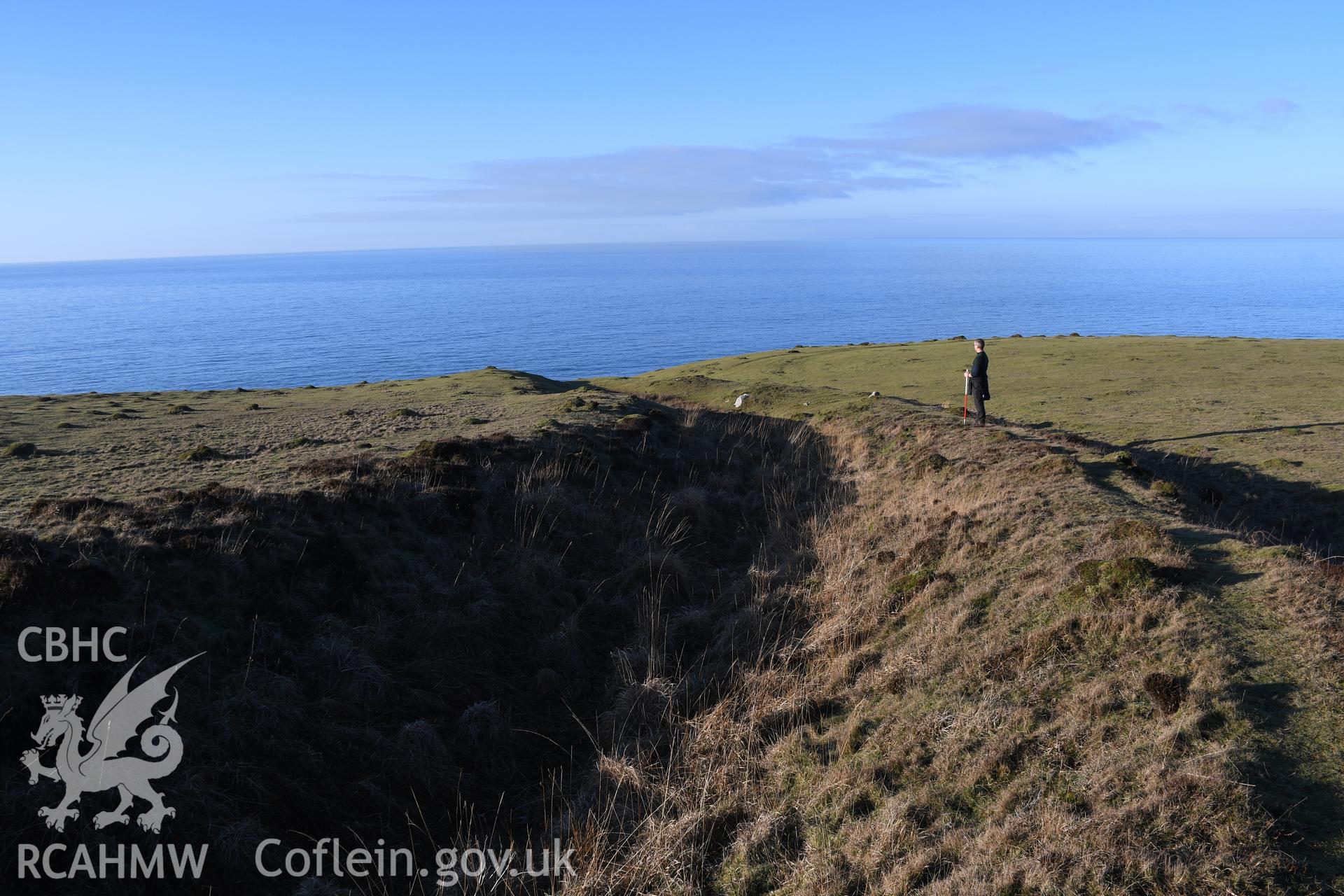 Inner ramparts with figure for scale, camera facing north. From photographic survey of Castell Bach promontory fort (NPRN 93914) using 1m scales and human figures. Undertaken by Hannah Genders Boyd for CHERISH project condition monitoring 13/01/2022.
Produced with EU funds through the Ireland Wales Co-operation Programme 2014-2020. All material made freely available through the Open Government Licence.