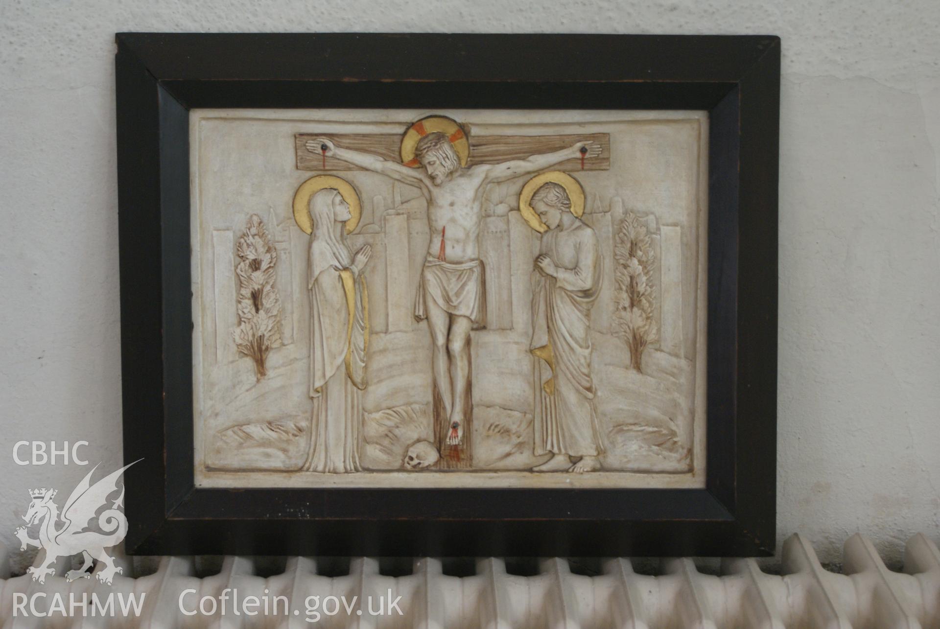 Digital colour photograph showing a framed painted plaster low-relief of the Crucifixion (believed to be by Margaret Agnes Rope), in the baptistry at Our Lady and St Michael Catholic church, Abergavenny.