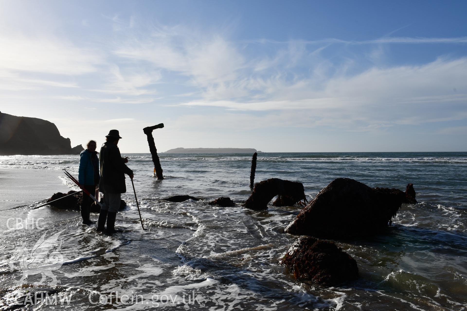 CHERISH team observing the wreck at low tide. Camera facing SW. Taken by Hannah Genders Boyd. Produced with EU funds through the Ireland Wales Co-operation Programme 2014-2023. All material made freely available through the Open Government Licence.