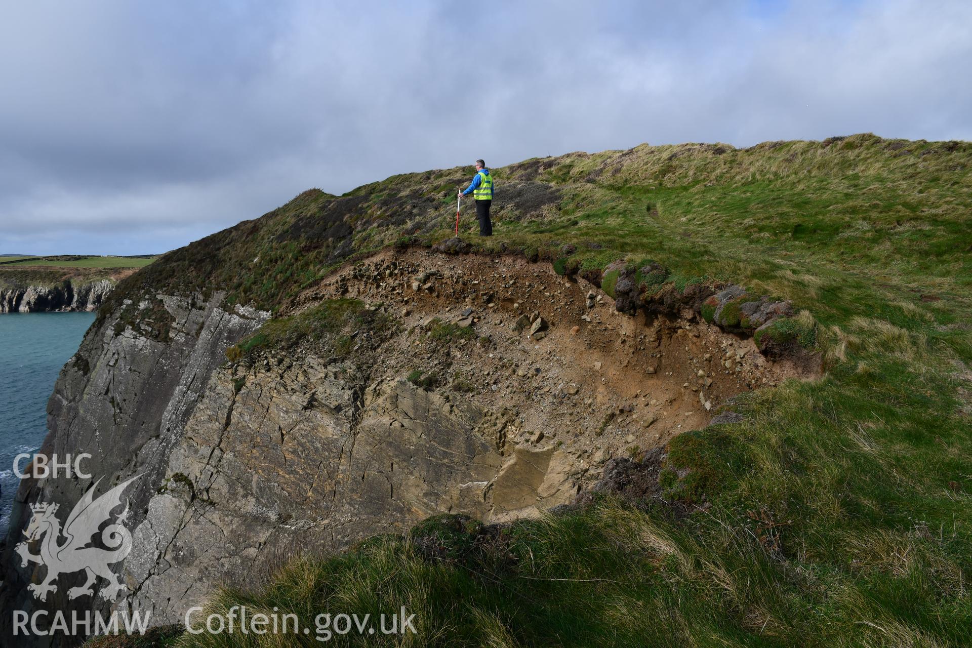 Eroding edge of site.  Camera facing NW. Person and 1m scale. Taken by Hannah Genders Boyd. Produced with EU funds through the Ireland Wales Co-operation Programme 2014-2023. All material made freely available through the Open Government Licence.