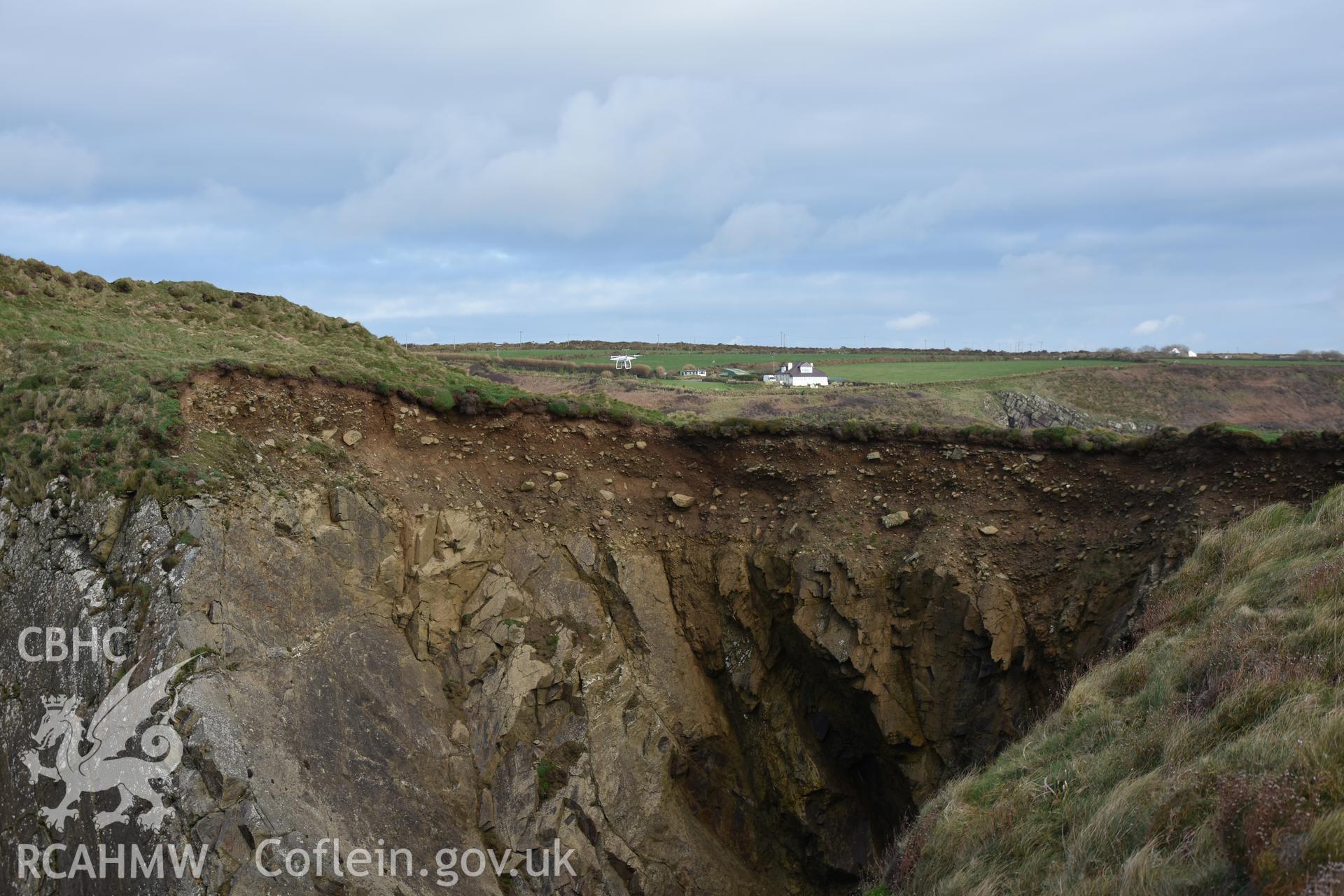 Eroding section through promontory fort Taken by Toby Driver. Produced with EU funds through the Ireland Wales Co-operation Programme 2014-2023. All material made freely available through the Open Government Licence.
