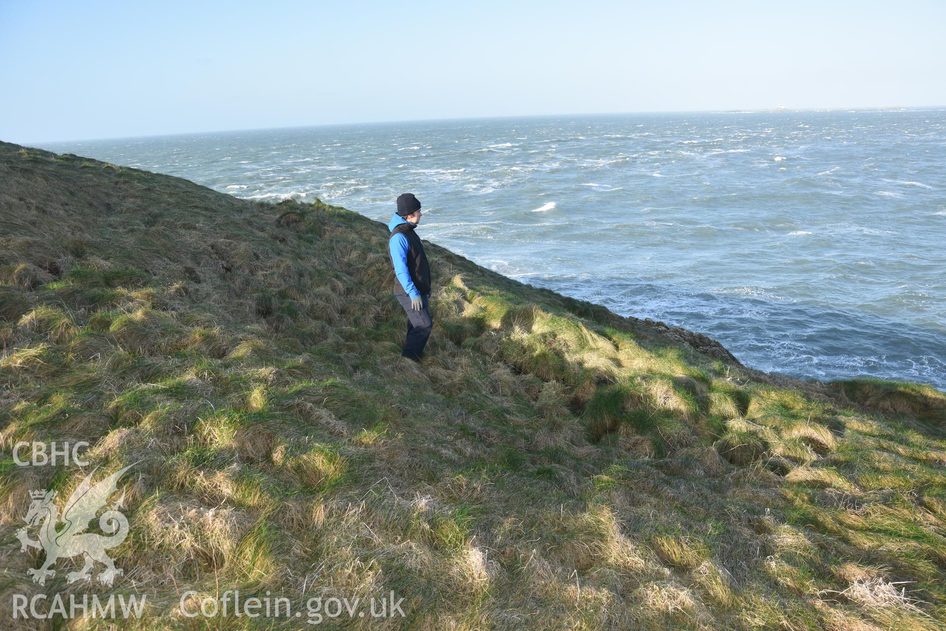 Ynys y Fydlym Hut Circle with figure for scale. Taken by Lou Barker. Produced with EU funds through the Ireland Wales Co-operation Programme 2014-2023. All material made freely available through the Open Government Licence.