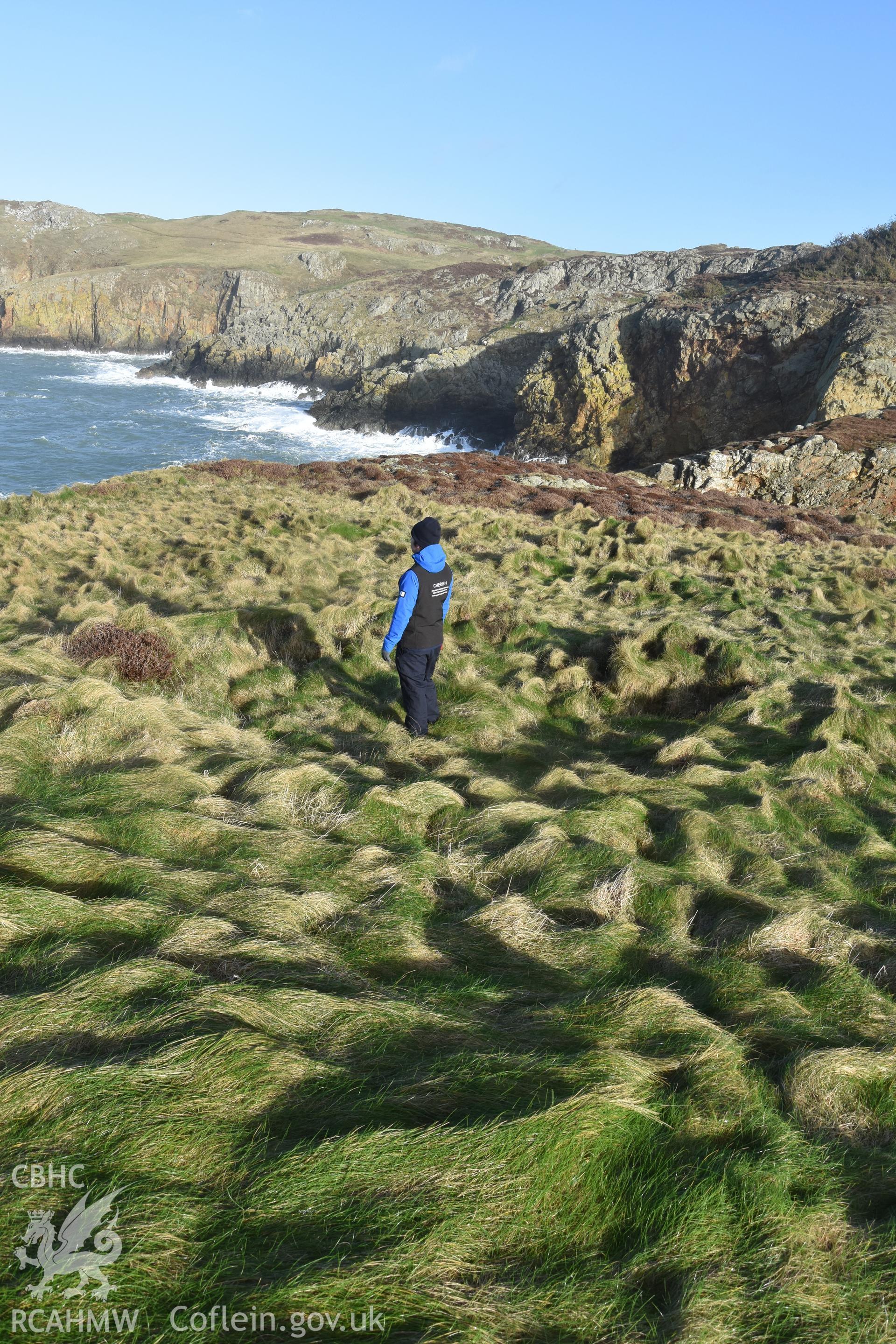 Ynys y Fydlym Hut Circle with figure for scale. Taken by Lou Barker. Produced with EU funds through the Ireland Wales Co-operation Programme 2014-2023. All material made freely available through the Open Government Licence.