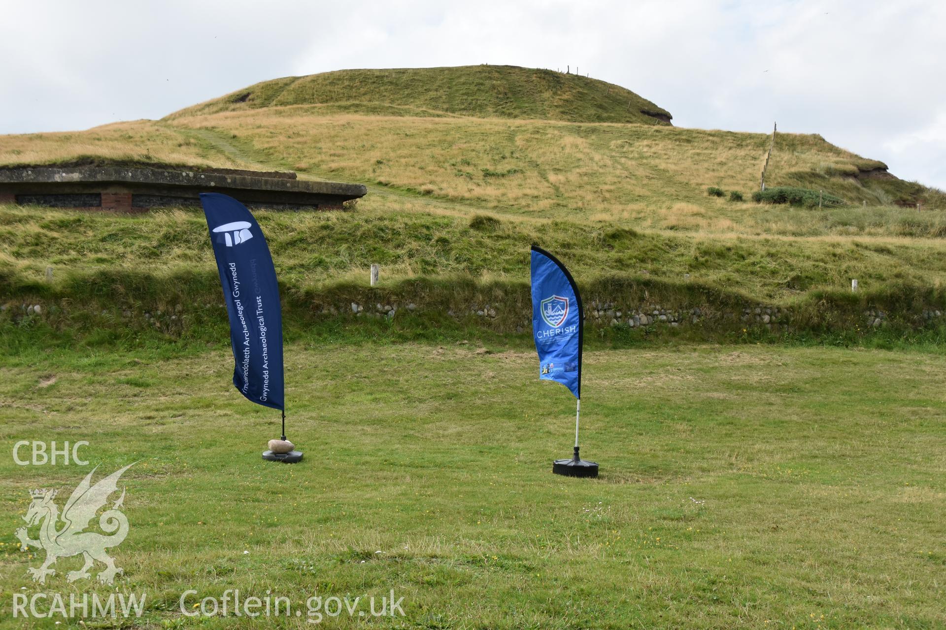 Flags at base of hillfort advertising excavation Taken by Toby Driver. Produced with EU funds through the Ireland Wales Co-operation Programme 2014-2023. All material made freely available through the Open Government Licence.