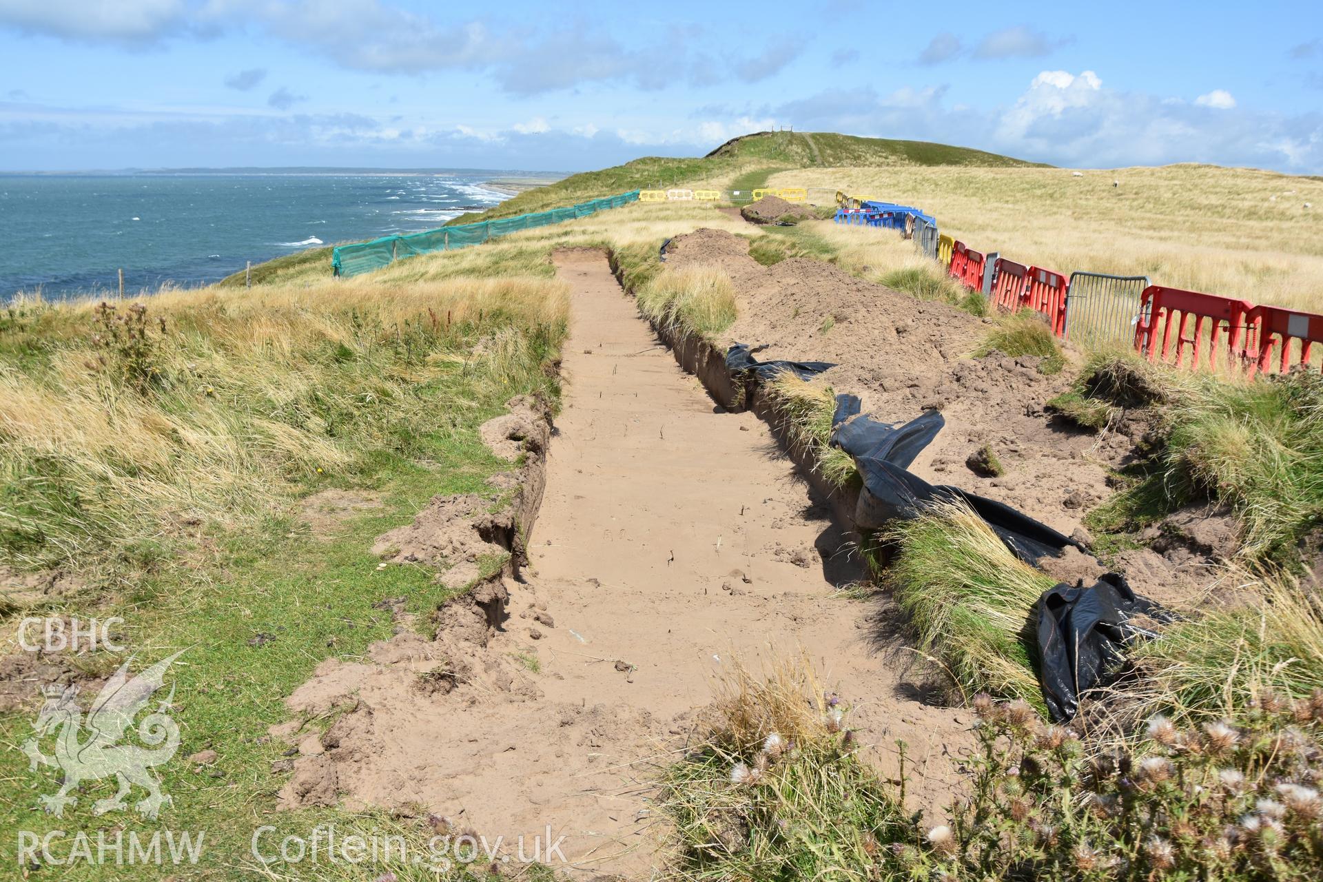 Open trench parallel to eroding cliff edge, showing layer of sand. Taken by Toby Driver. Produced with EU funds through the Ireland Wales Co-operation Programme 2014-2023. All material made freely available through the Open Government Licence.