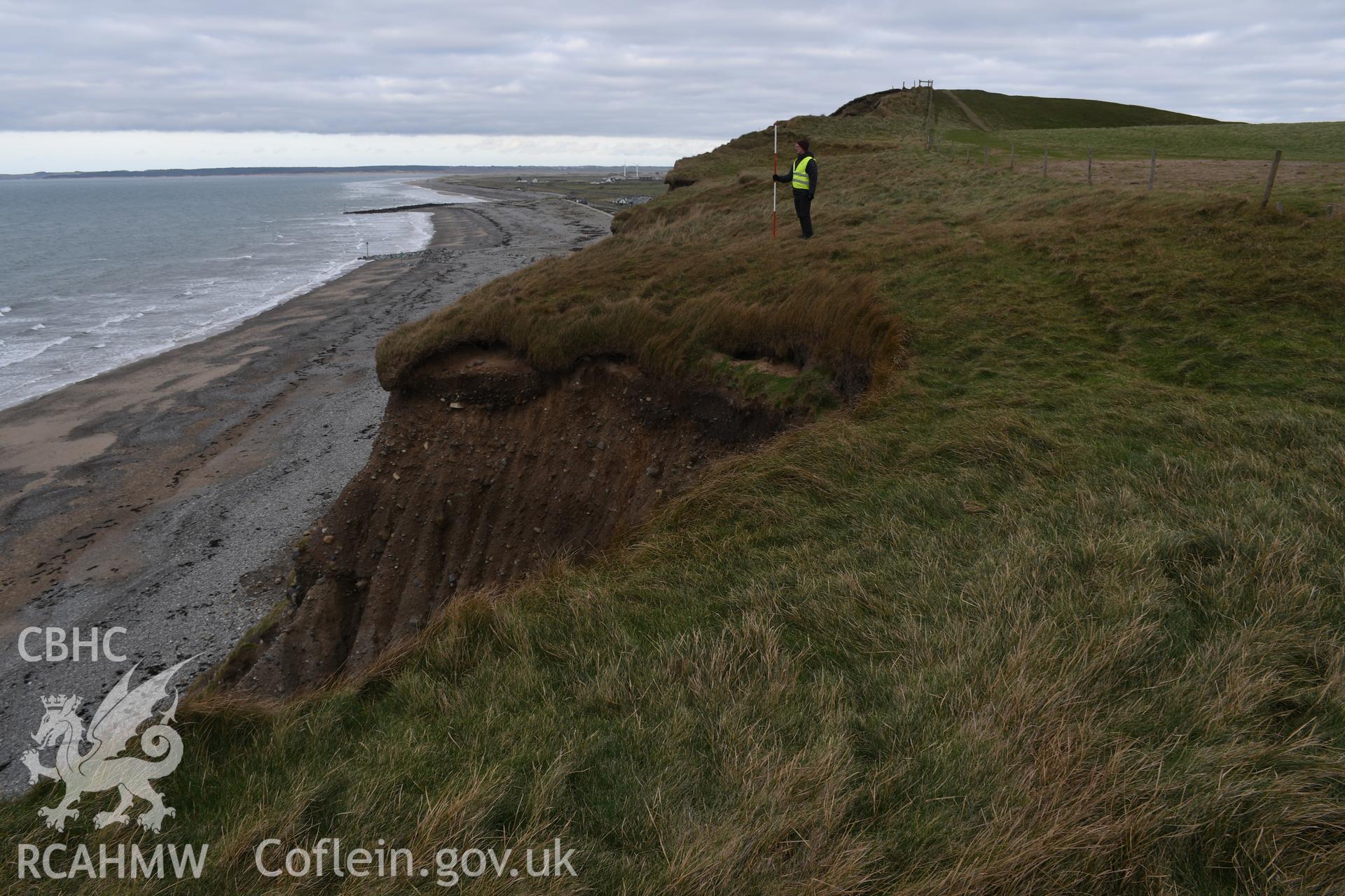 Looking north along eroding coast. Figure and 2m scale. Taken by Hannah Genders Boyd. Produced with EU funds through the Ireland Wales Co-operation Programme 2014-2023. All material made freely available through the Open Government Licence.