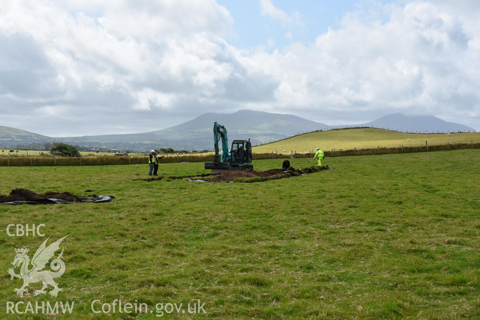 Mechanical digger opening trench with archaeologists supervising. Taken by Toby Driver. Produced with EU funds through the Ireland Wales Co-operation Programme 2014-2023. All material made freely available through the Open Government Licence.