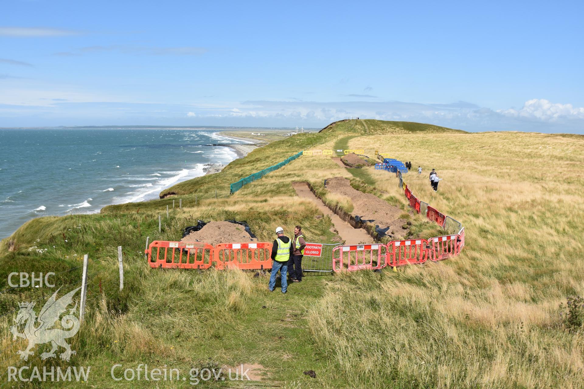 View north showing hillfort and open trench with archaeologists supervising preparations for hand excavation. Taken by Toby Driver. Produced with EU funds through the Ireland Wales Co-operation Programme 2014-2023. All material made freely available throu