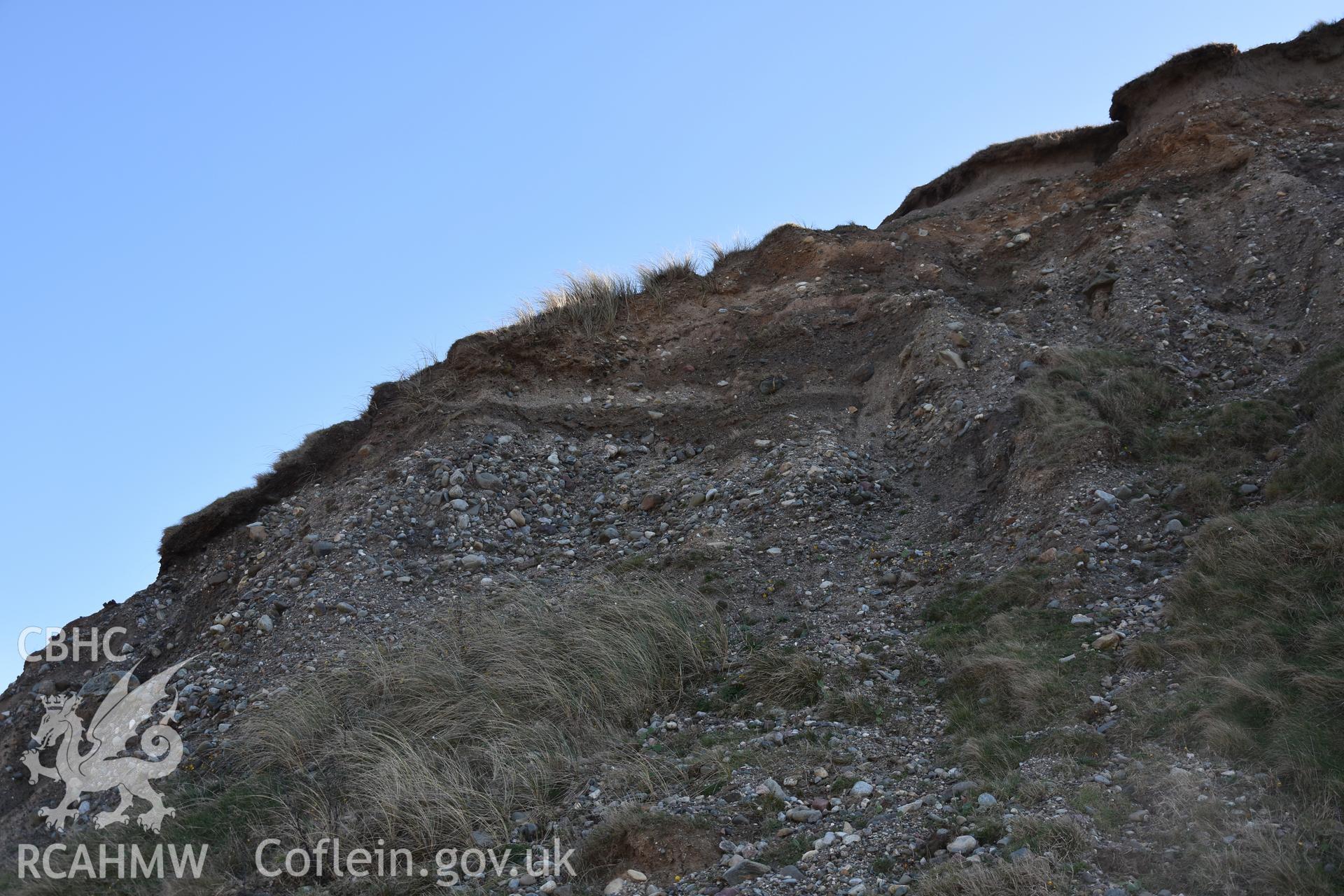 Close up shot of eroding cliff face from underneath. Grassy tufts and stratigraphy at the top visisble. Taken by Toby Driver. Produced with EU funds through the Ireland Wales Co-operation Programme 2014-2023. All material made freely available through the