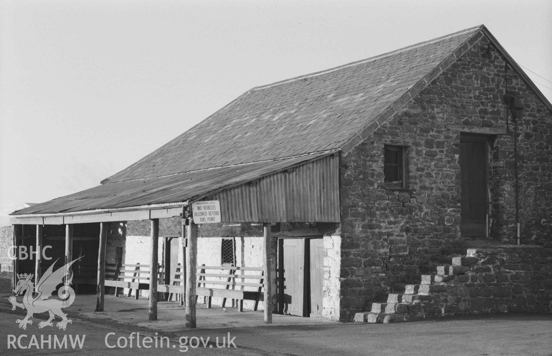 Digital copy of a black and white negative showing view of the old stone building and wooden shelter on the north west side of the Harbourmaster Inn, Quay Parade, Aberaeron. Photographed by Arthur Chater on 28 December 1968. Looking north west from Grid Reference SN 4557 6297.