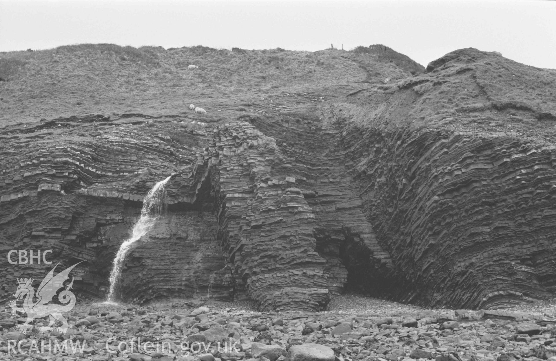 Digital copy of a black and white negative showing Ffos y Ffin emerging from Cwm Gilfach onto the beach; low tide. Photographed by Arthur Chater on 3 January 1969. Looking south east from Grid Reference SN 4388 6175.