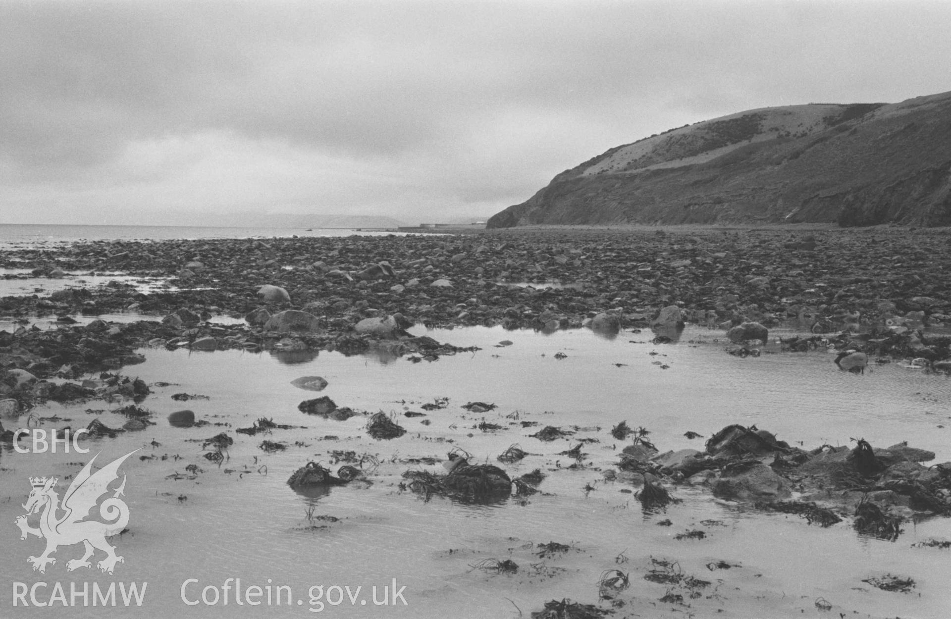 Digital copy of a black and white negative showing view up the coast from opposite Cwm Gilfach towards Aberaeron at low tide. Photographed by Arthur Chater on 3 January 1969. Looking north east from Grid Reference SN 4388 6178.