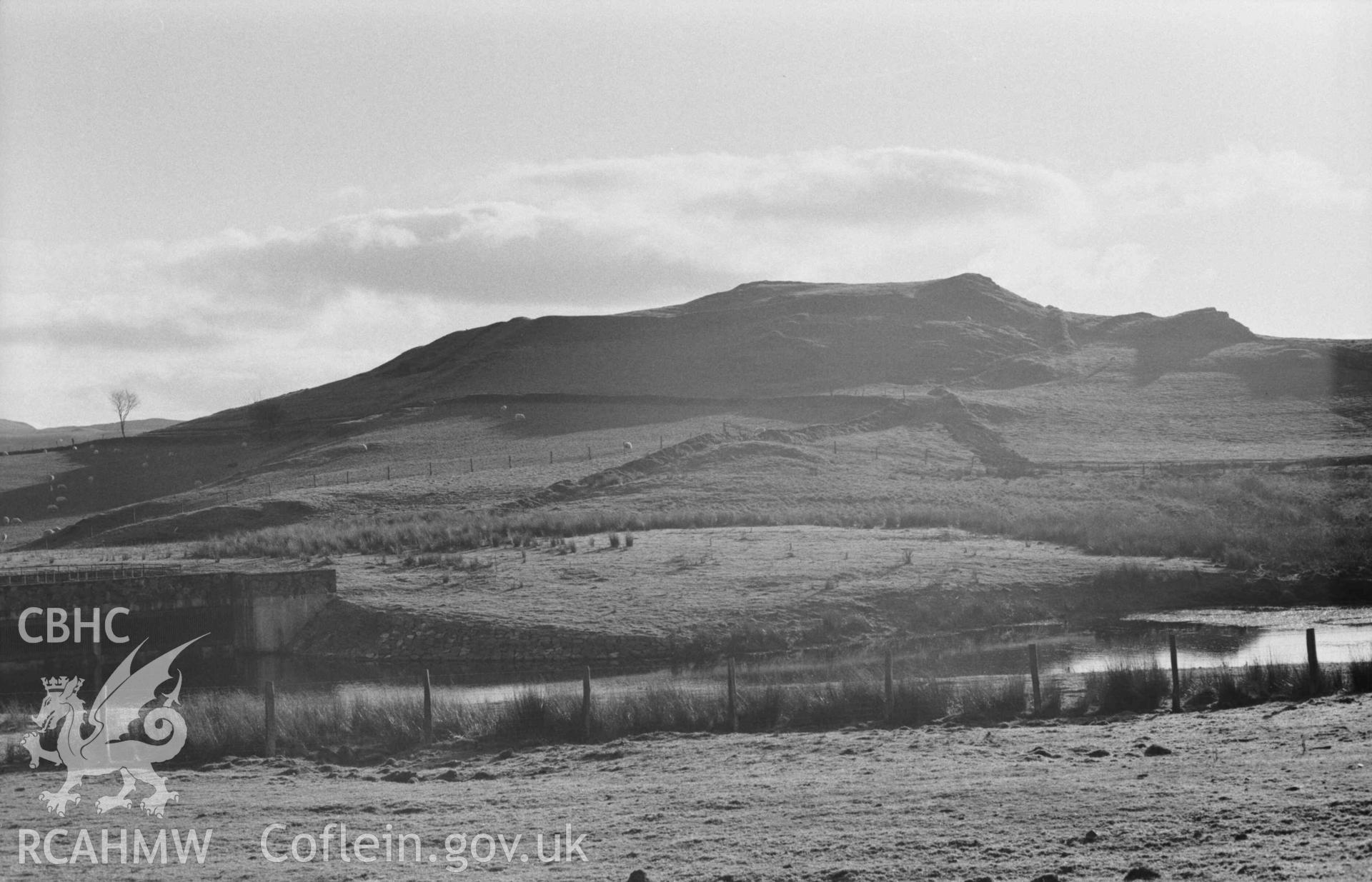 Digital copy of a black and white negative showing Castell Bwa Drain iron age camp, seen across the small reservoir pond 150m west of the farm. Photographed by Arthur Chater on 5 January 1969. Looking south from Grid Reference SN 7133 7973.