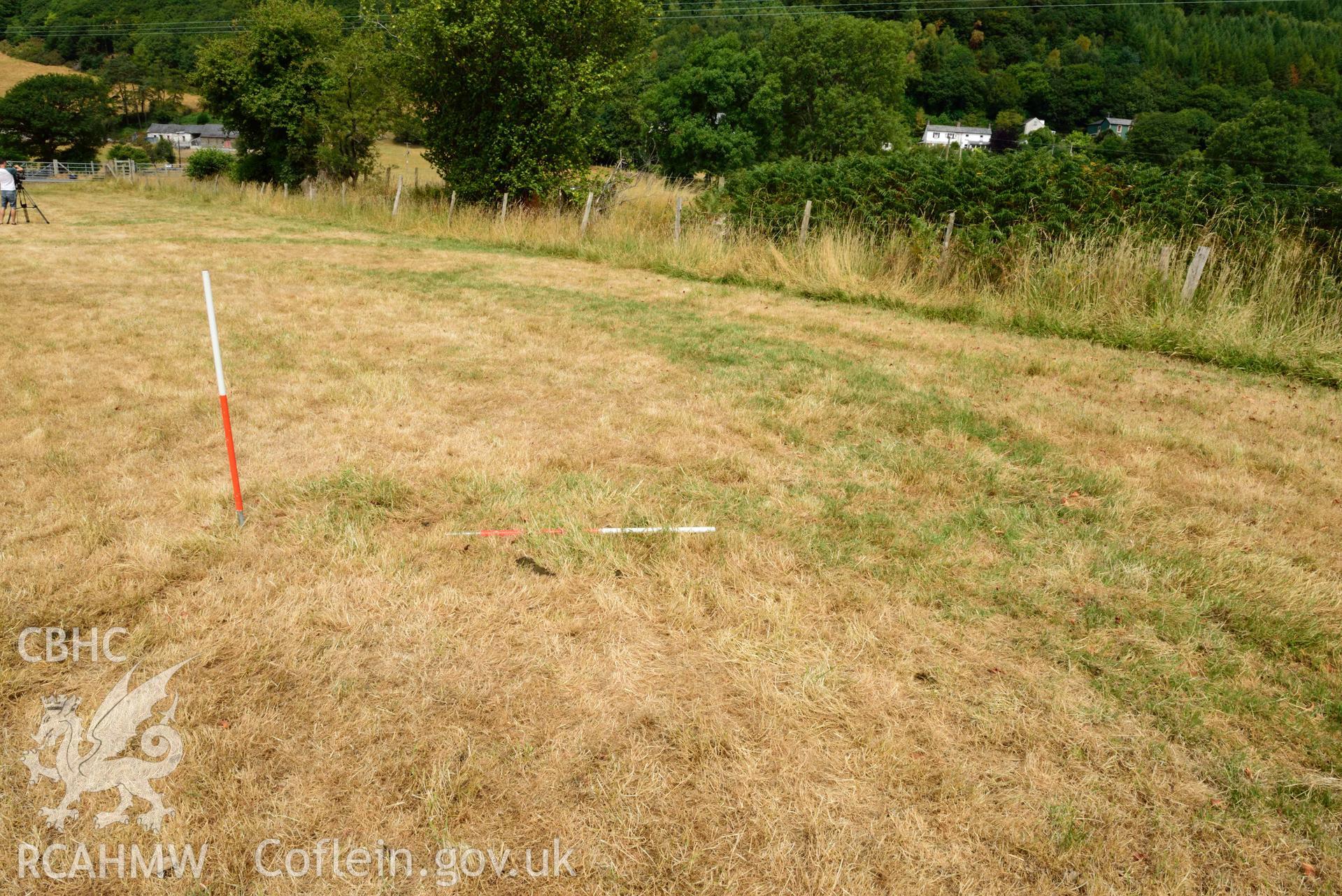 View of rectangular pit inside concentric barrow, against eastern inner ditch, looking North East (scale 1m) at Dollwen barrow cemetery. Photographed by Toby Driver of RCHMAW during BBC filming of The One Show, 17 July 2018. Associated with Geophysical Survey of Pen y Wal, Dollwen Barrow, Goginan, commissioned by the RCAHMW and produced by Sumo Survey, 2021.