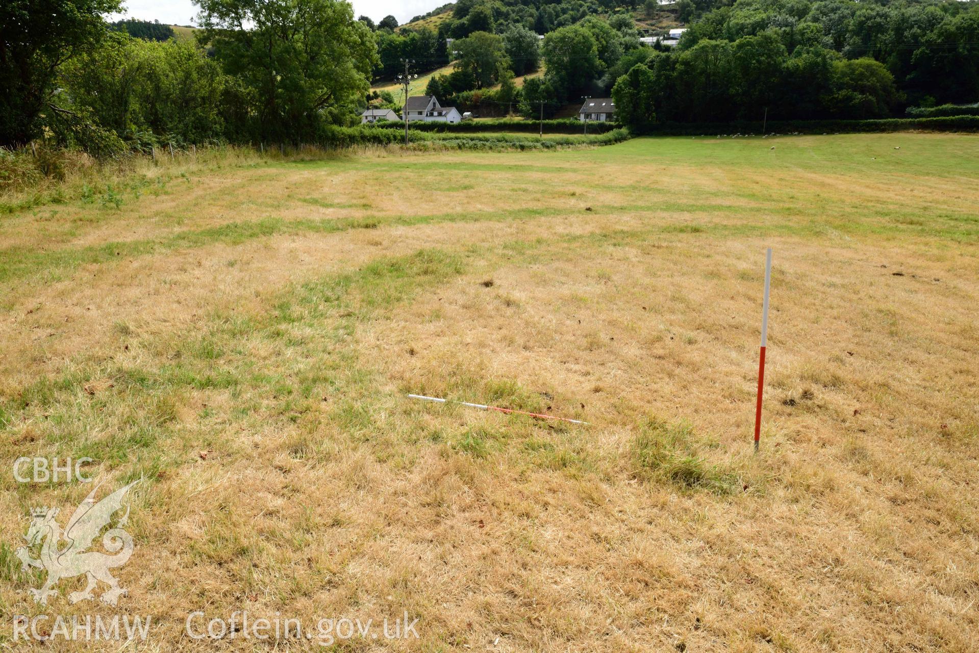 View of rectangular pit inside concentric barrow, against eastern inner ditch, looking South East (scale 1m) at Dollwen barrow cemetery. Photographed by Toby Driver of RCHMAW during BBC filming of The One Show, 17 July 2018. Associated with Geophysical Survey of Pen y Wal, Dollwen Barrow, Goginan, commissioned by the RCAHMW and produced by Sumo Survey, 2021.