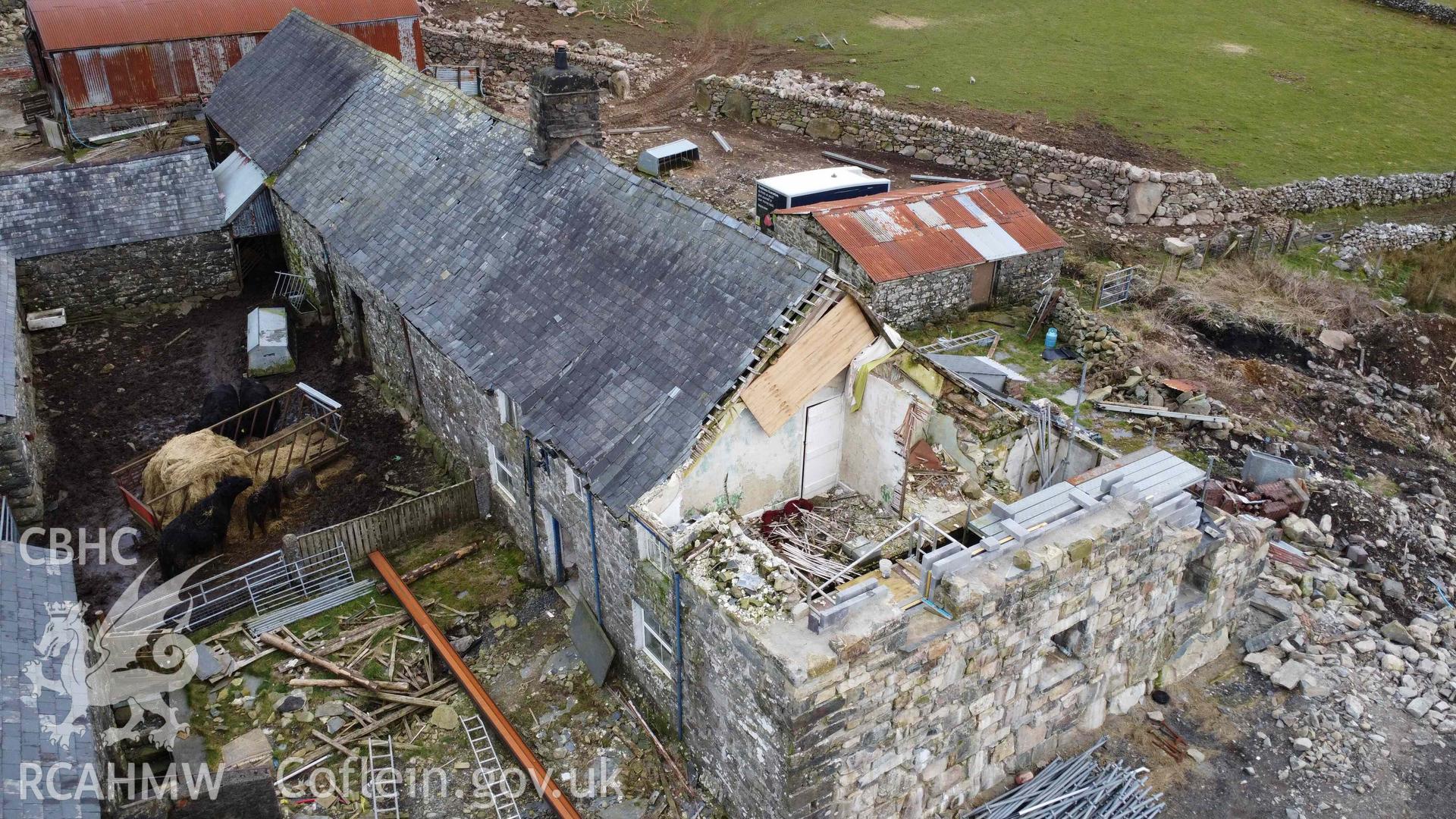 Aerial view of the boarded up western gable end of Tyddyn Mawr farmhouse. The wall was taken down due to instability, exposing the gable end truss, which was boarded over to protect it from the elements. Part of a photographic survey of Tyddyn Mawr farmhouse, Trawsfynydd, conducted by Dr Jayne Kamintzis of RCAHMW on 13 June 2023.