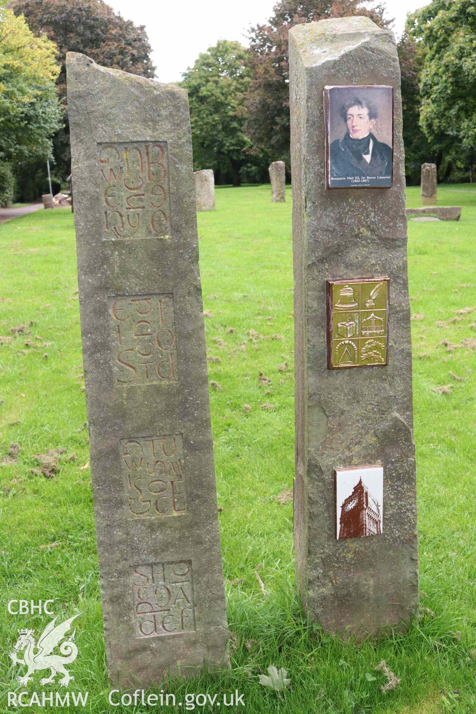 Photograph showing view of standing stone at Gorsedd Circle stone at Abergavenny. One of twin stones installed in 2009 to commemorate Lady and Lord Lanover and their work to promote Welsh language and customs, featuring artwork by Jane Turner and Ned Heywood. This stone shows Benjamin Hall (Lord Lanover), and representative images, including Big Ben, named after him.